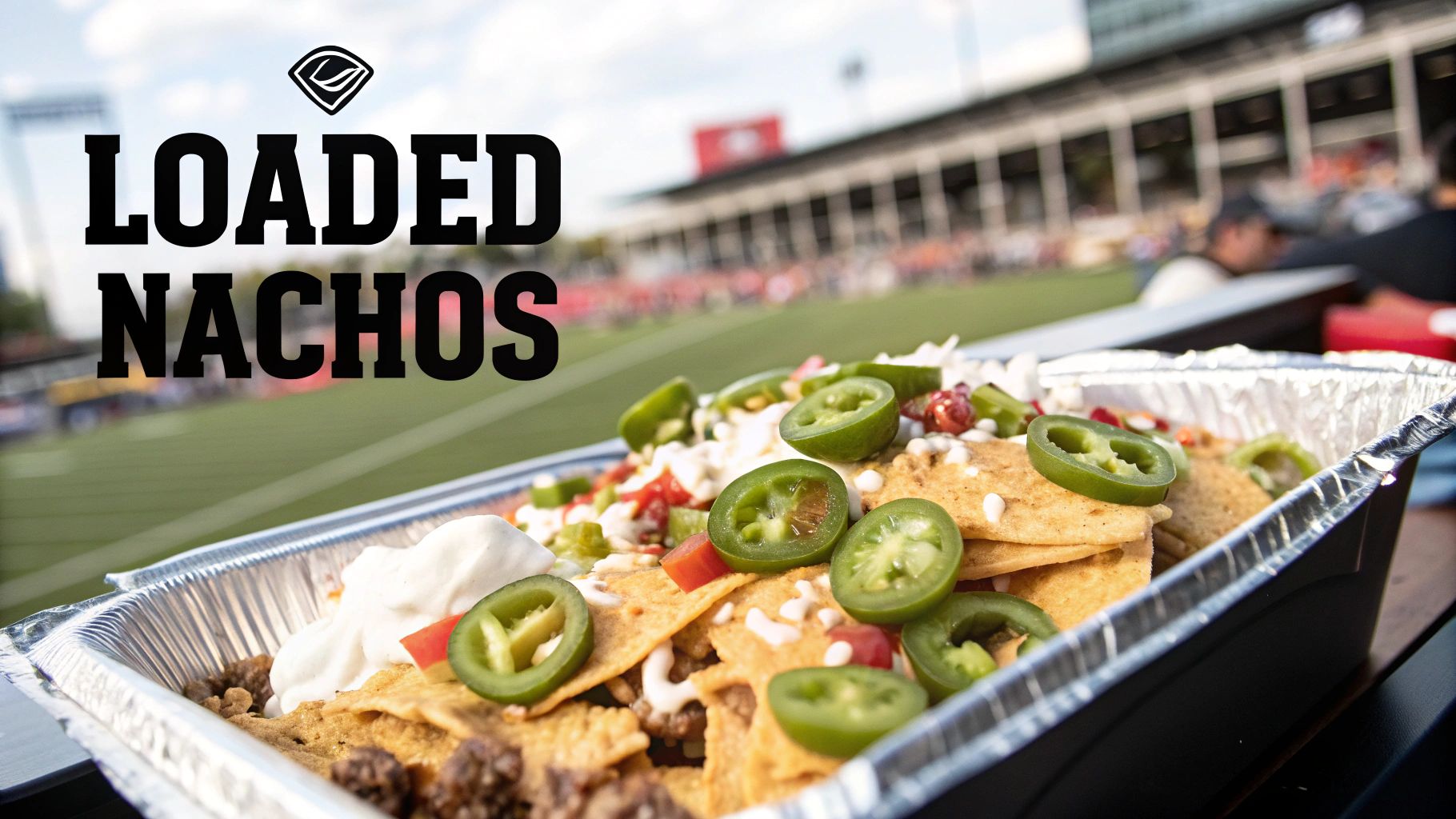 Delicious loaded nachos with meat, cheese, sour cream, and jalapeños in a foil container at a sports stadium.