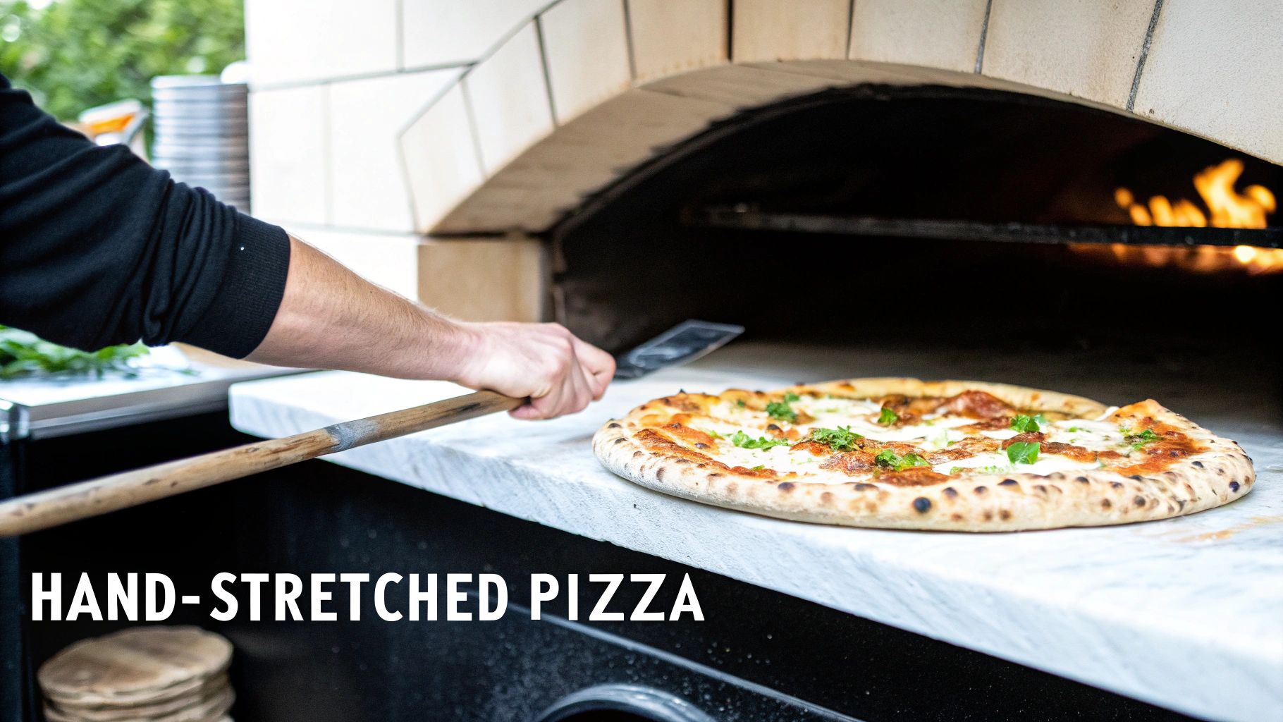 A chef slides a freshly baked pizza with basil from a traditional wood-fired oven onto a counter.