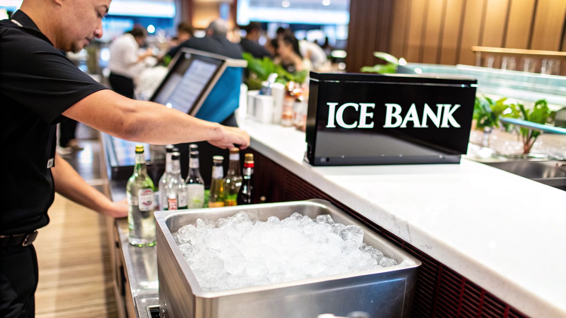 A person prepares drinks at a bar counter, next to a large stainless steel ice bin and an 'ICE BANK' sign.