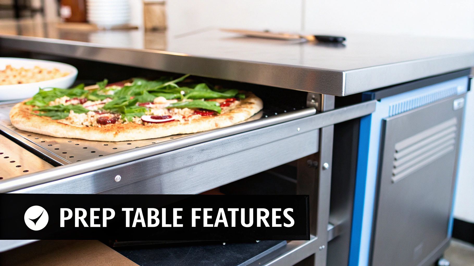 Freshly topped pizza with greens and ingredients on a perforated pan in a stainless steel commercial prep table.