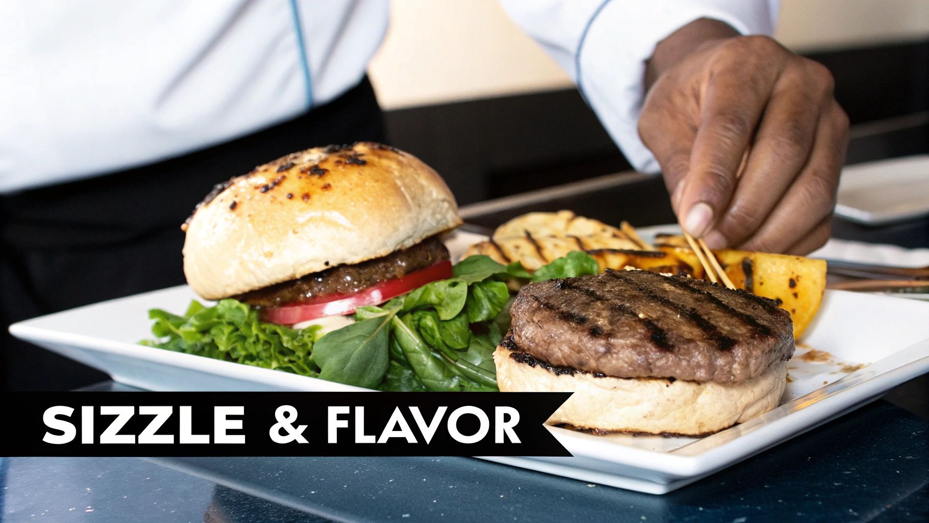 A chef's hand garnishes two gourmet burgers with fresh lettuce, tomato, and grilled potatoes on a white plate.