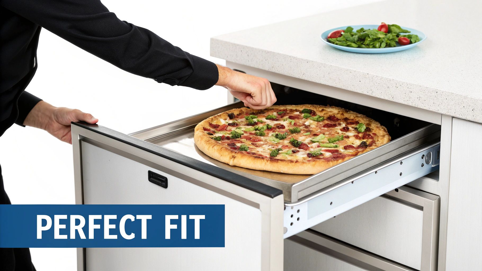 Person placing a large pepperoni and broccoli pizza on a metal tray into an open undercounter drawer, with a salad nearby.