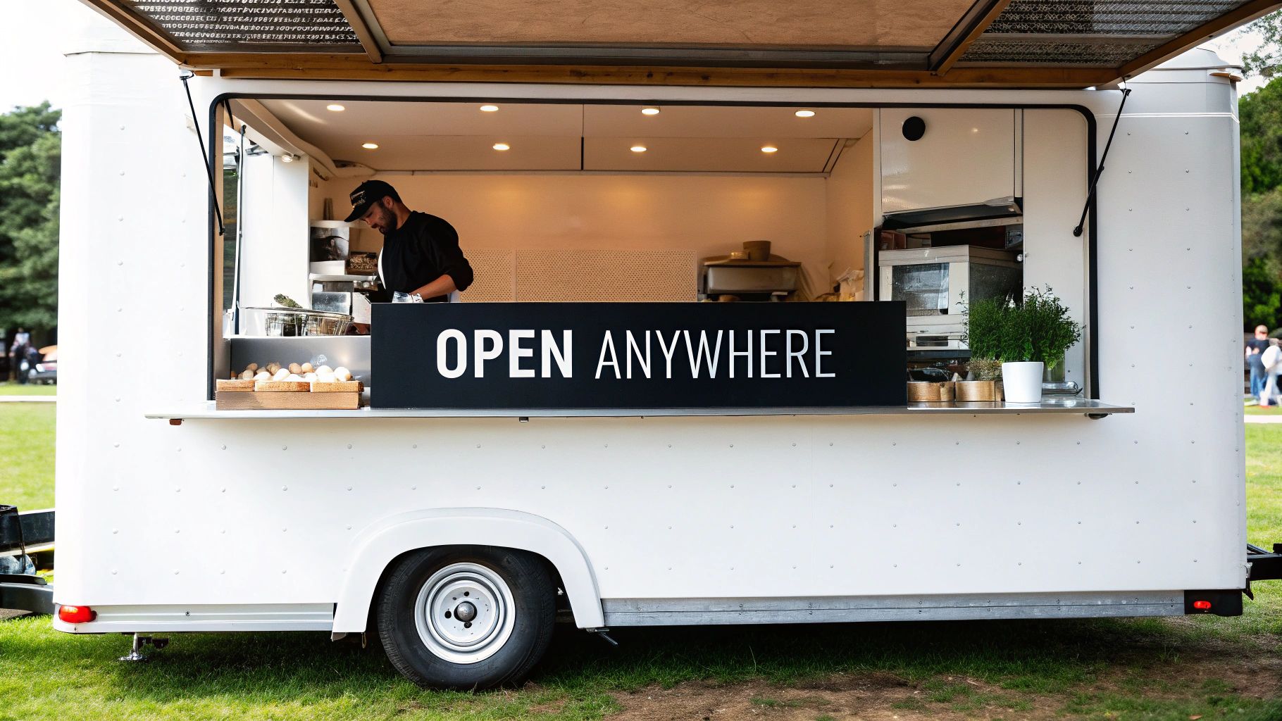 A white food truck with an 'OPEN ANYWHERE' sign, a chef preparing food inside.