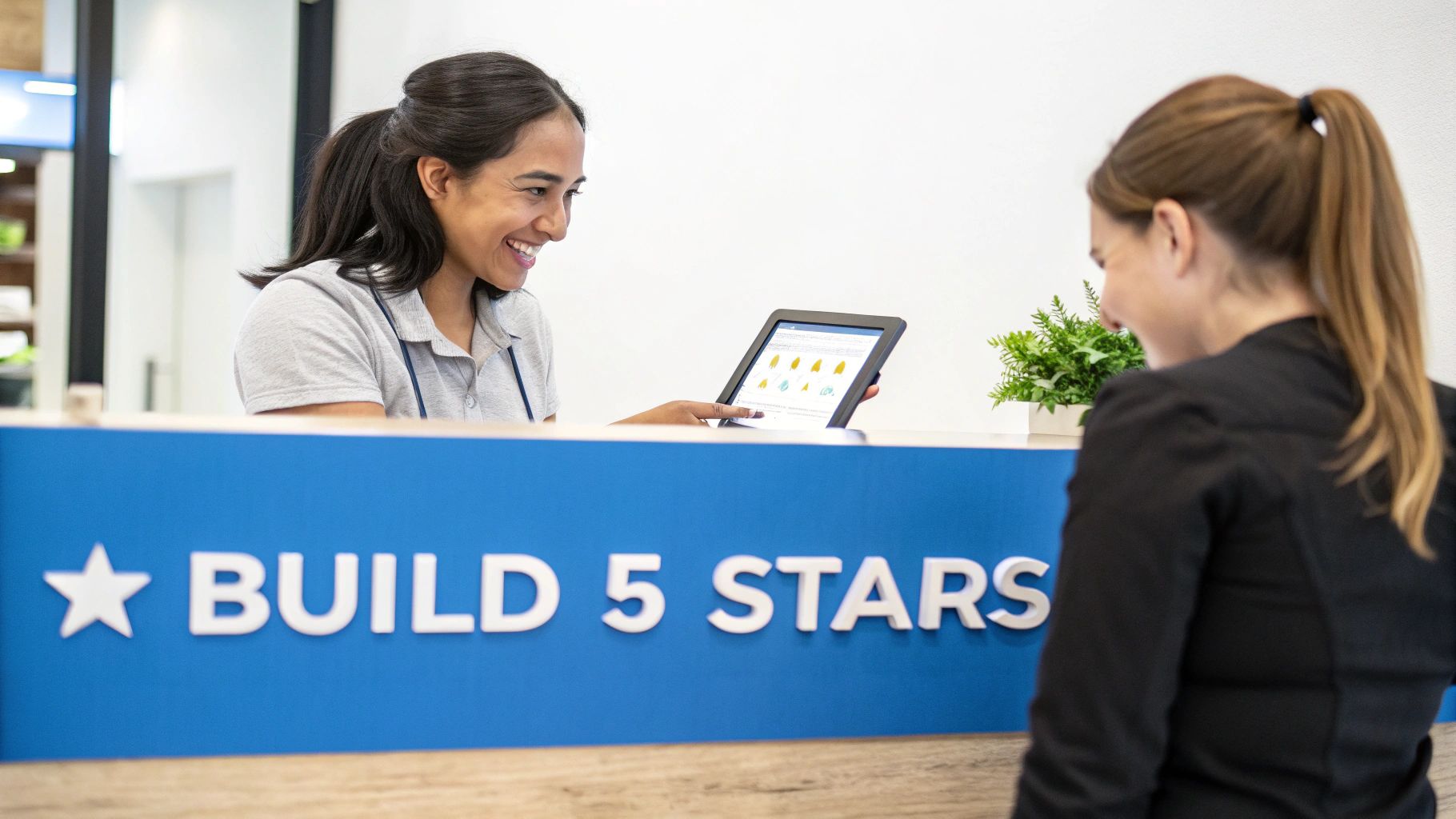 A smiling woman shows performance data on a tablet to a client at a "BUILD 5 STARS" counter.