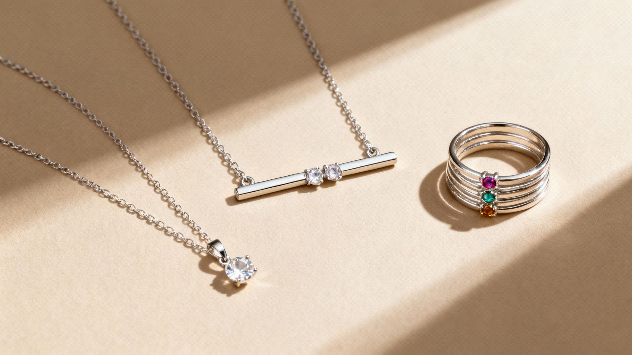 Silver necklaces with clear stone pendants and a stackable silver ring featuring colorful birthstones.