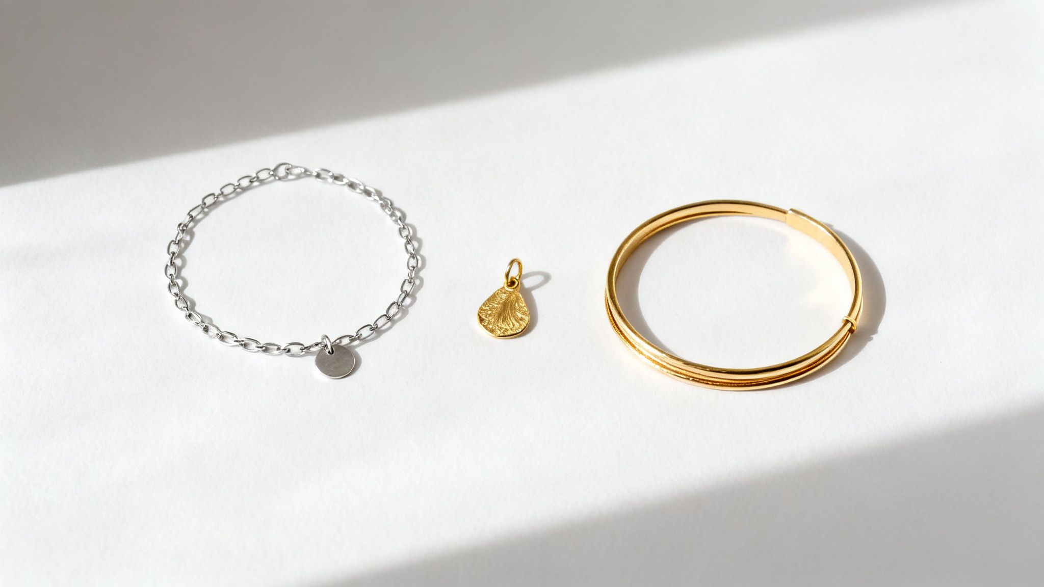 Three pieces of jewelry, including a silver bracelet, a gold pendant, and a gold bangle, on a white surface.