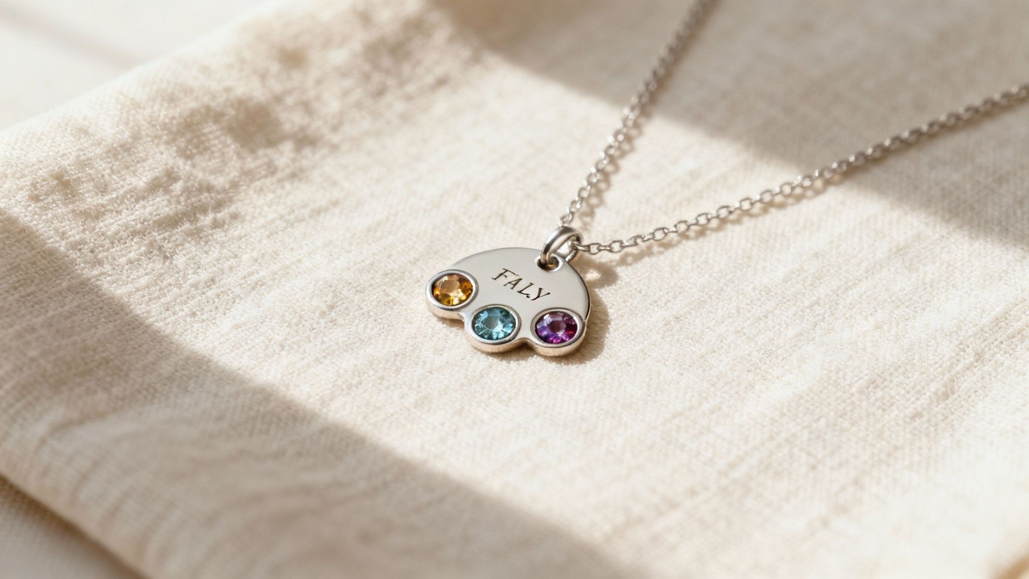 Personalized silver pendant necklace with three colorful birthstones and engraved family name on white fabric