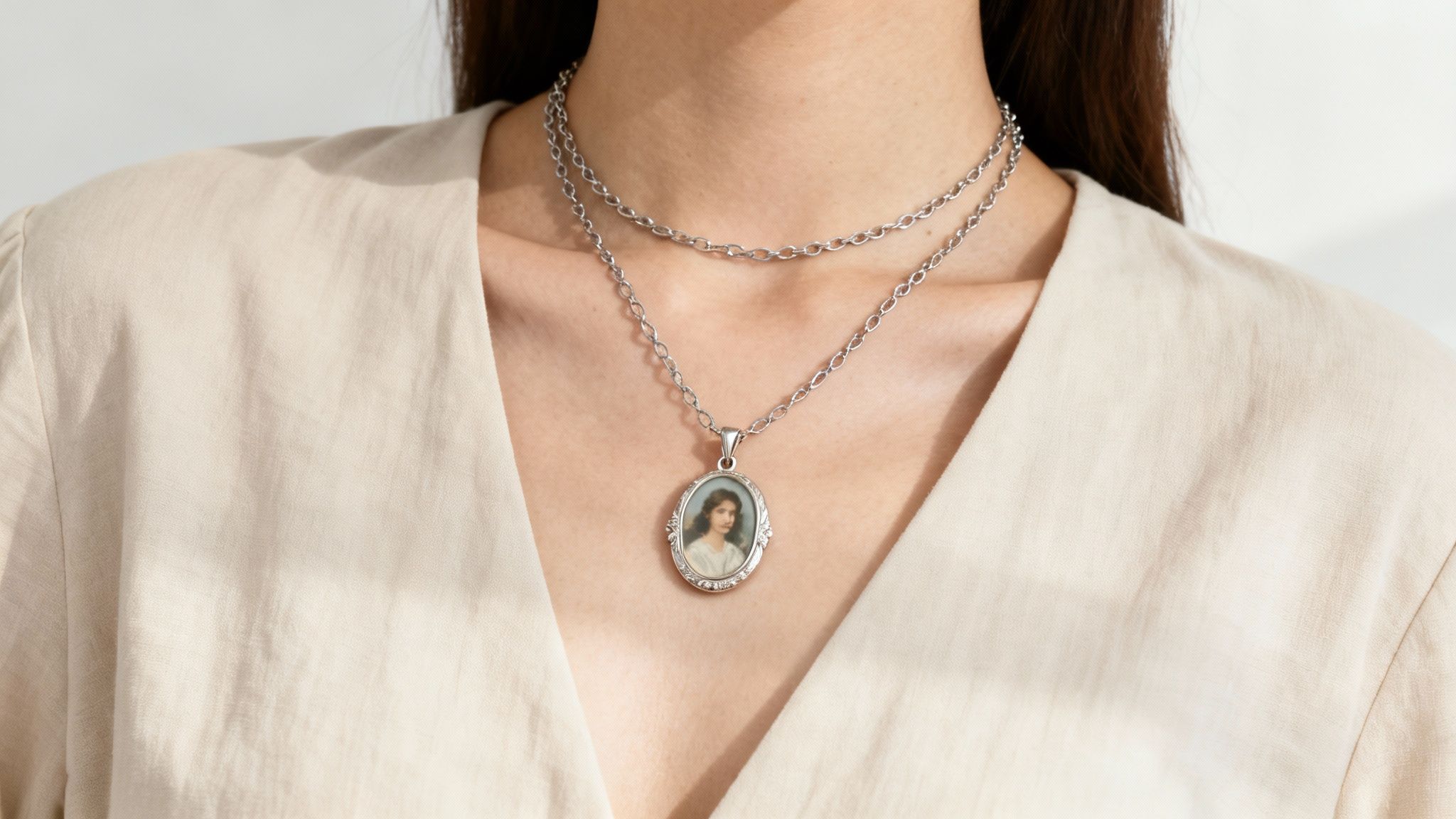 A woman wearing a layered necklace set that includes a delicate gold locket, complemented by a simple V-neck top.