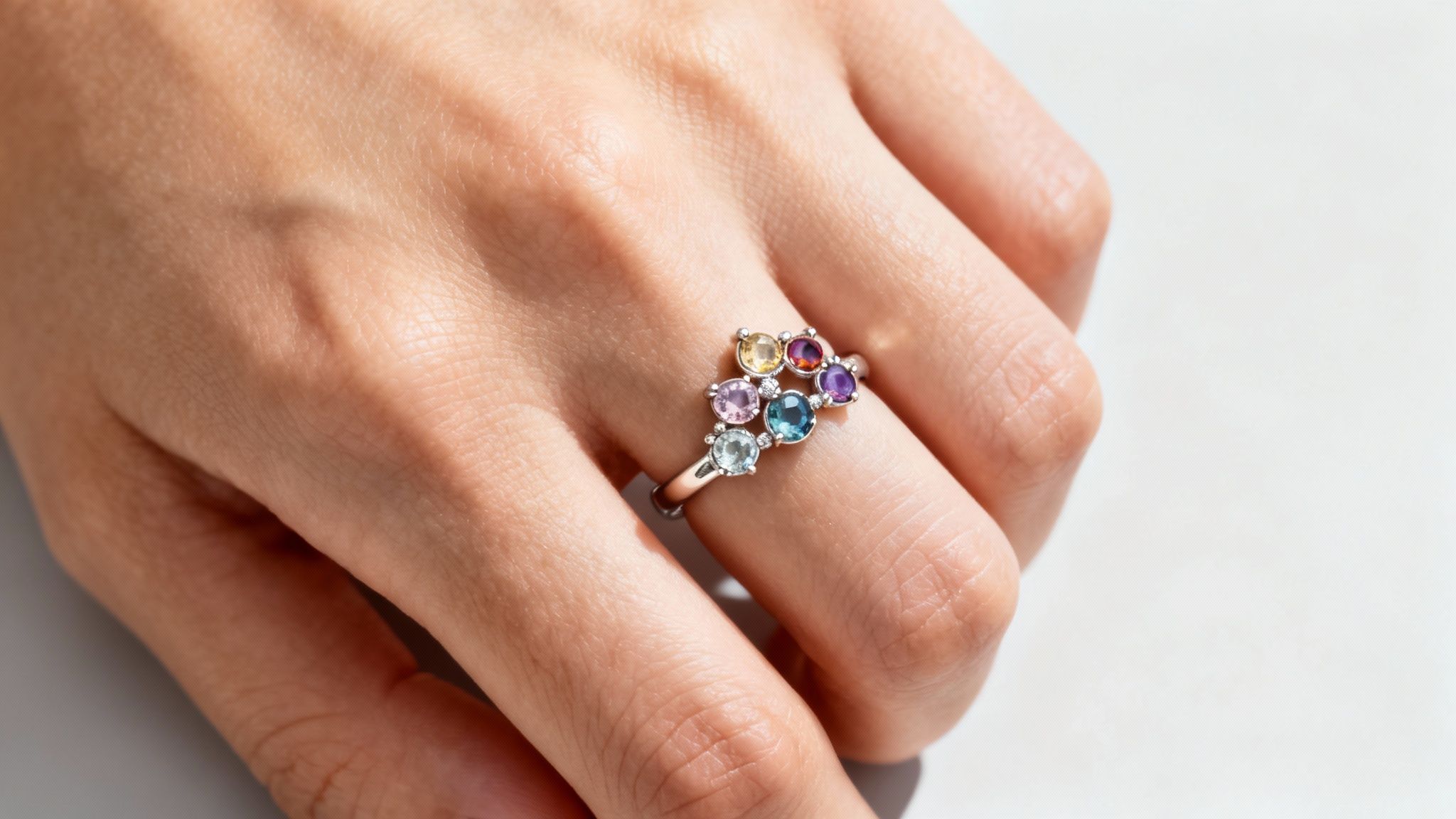A close-up of a hand wearing a silver mothers ring with a cluster of colorful gemstones.