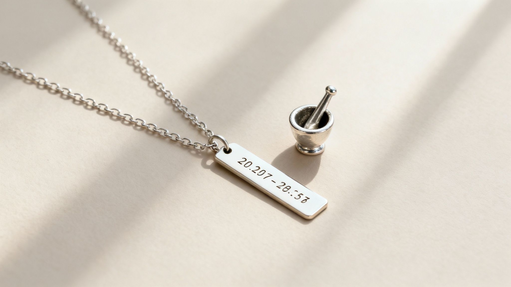 A silver necklace with an engraved bar pendant lies next to a miniature mortar and pestle.