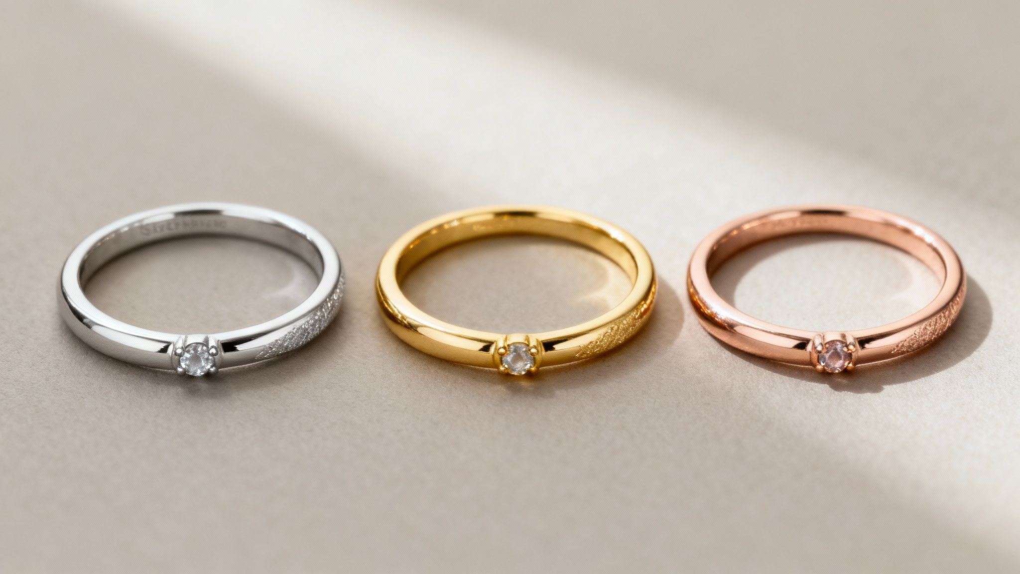 Three elegant engagement rings in silver, gold, and rose gold with small gemstones