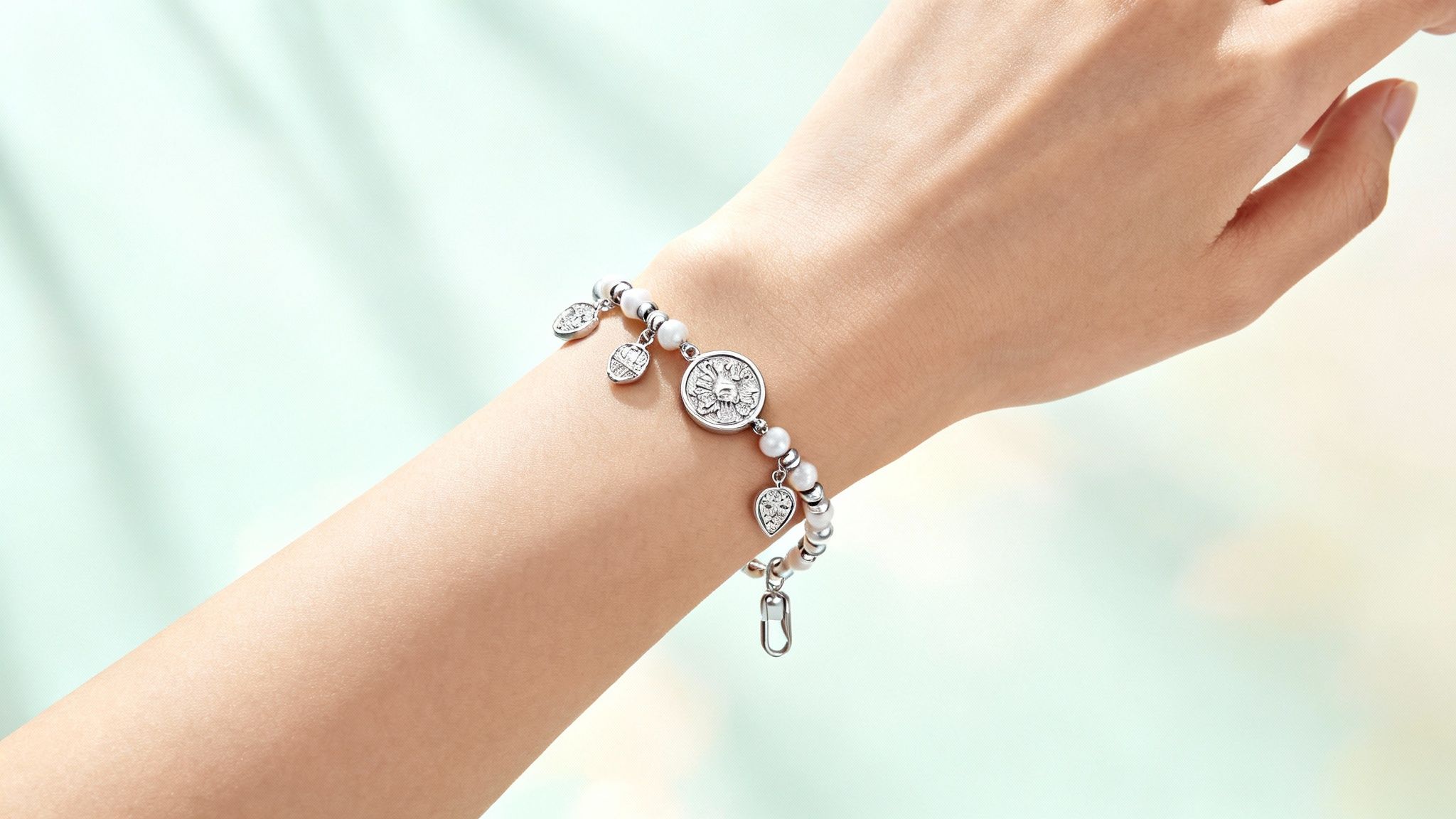 A hand holds a charm bracelet, showcasing a mix of silver charms against a soft background.
