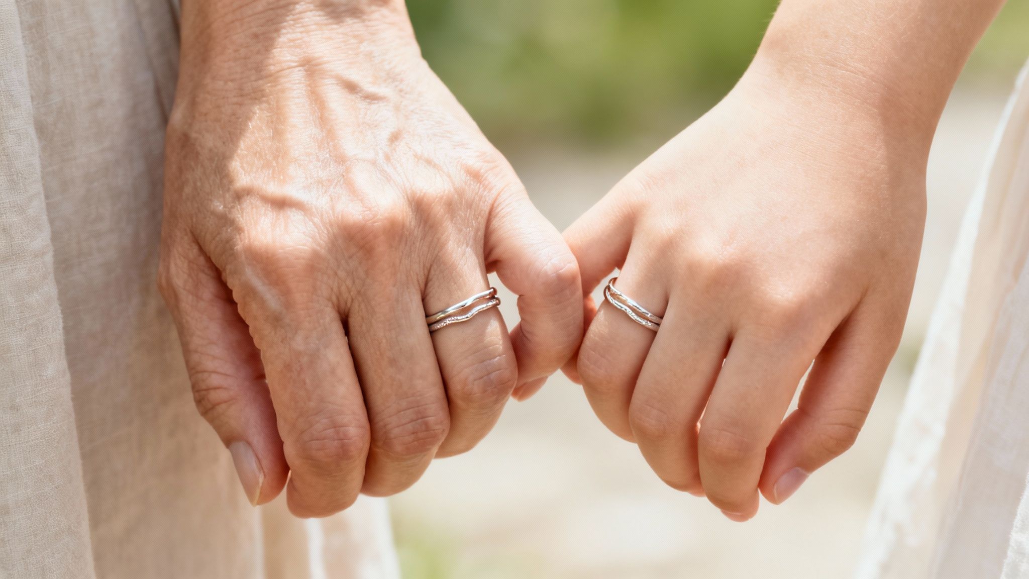 Two hands, one older and one younger, wearing matching rings and holding each other gently