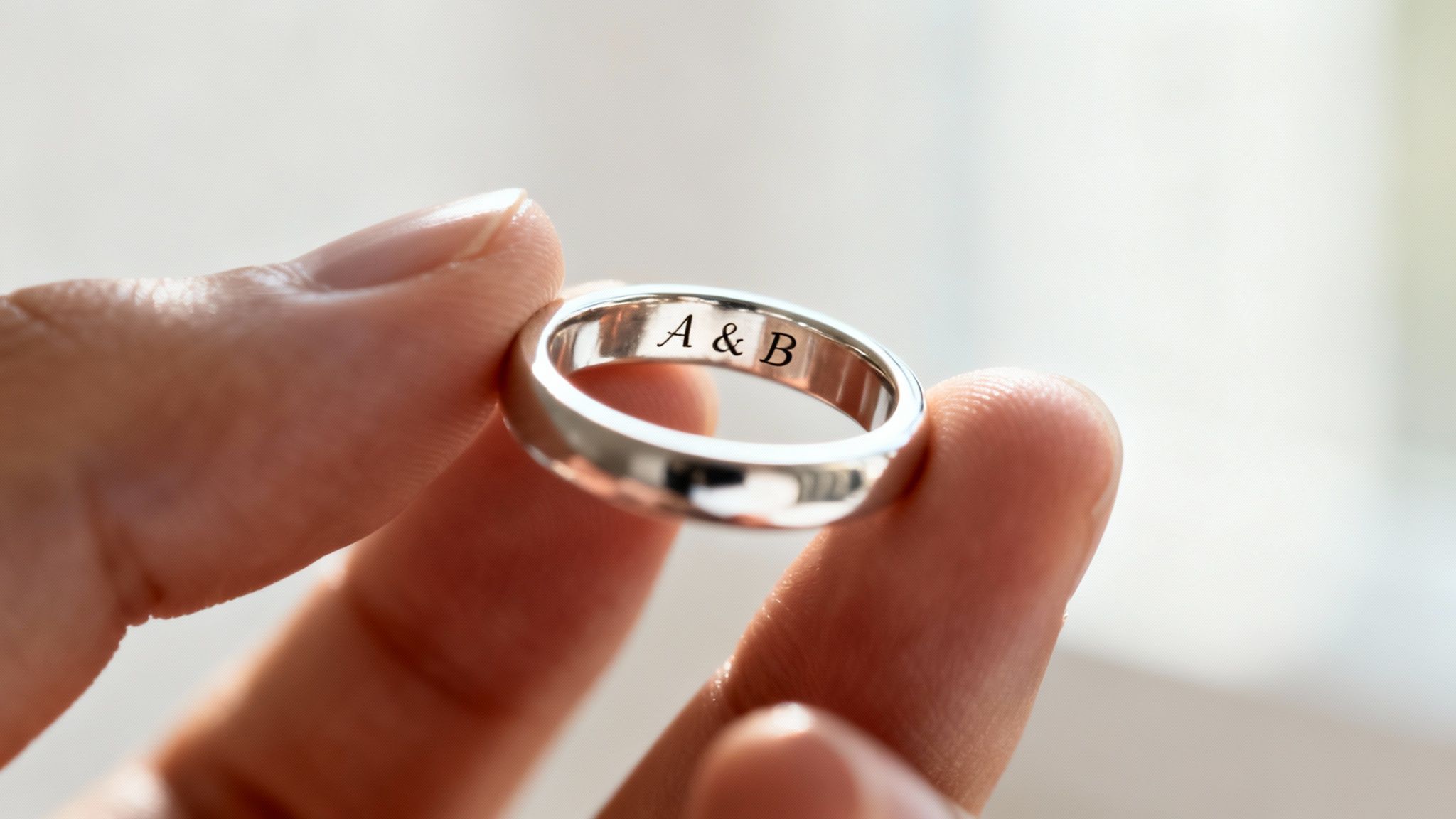 A person's hand holds a silver ring engraved with the initials 'A & B'.