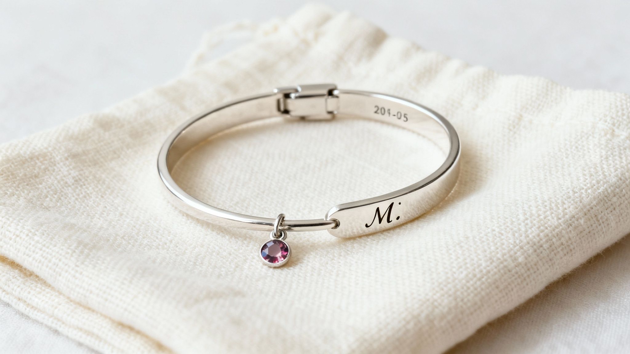 Close-up of an elegant silver bangle bracelet with a sparkling purple charm on a soft fabric pouch.