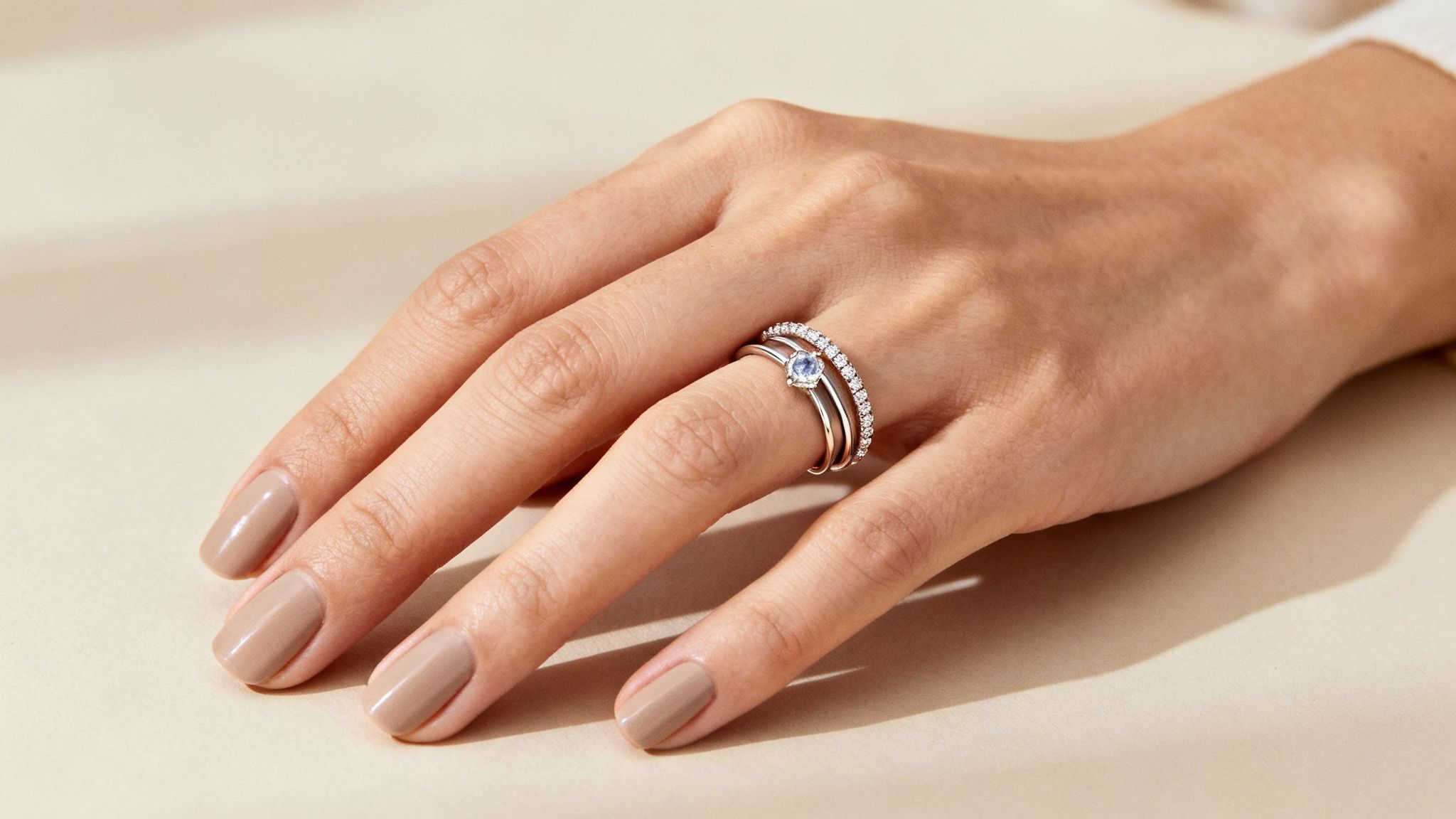 A person's hand showcasing a stack of three elegant rings, including a blue birthstone and diamond band.