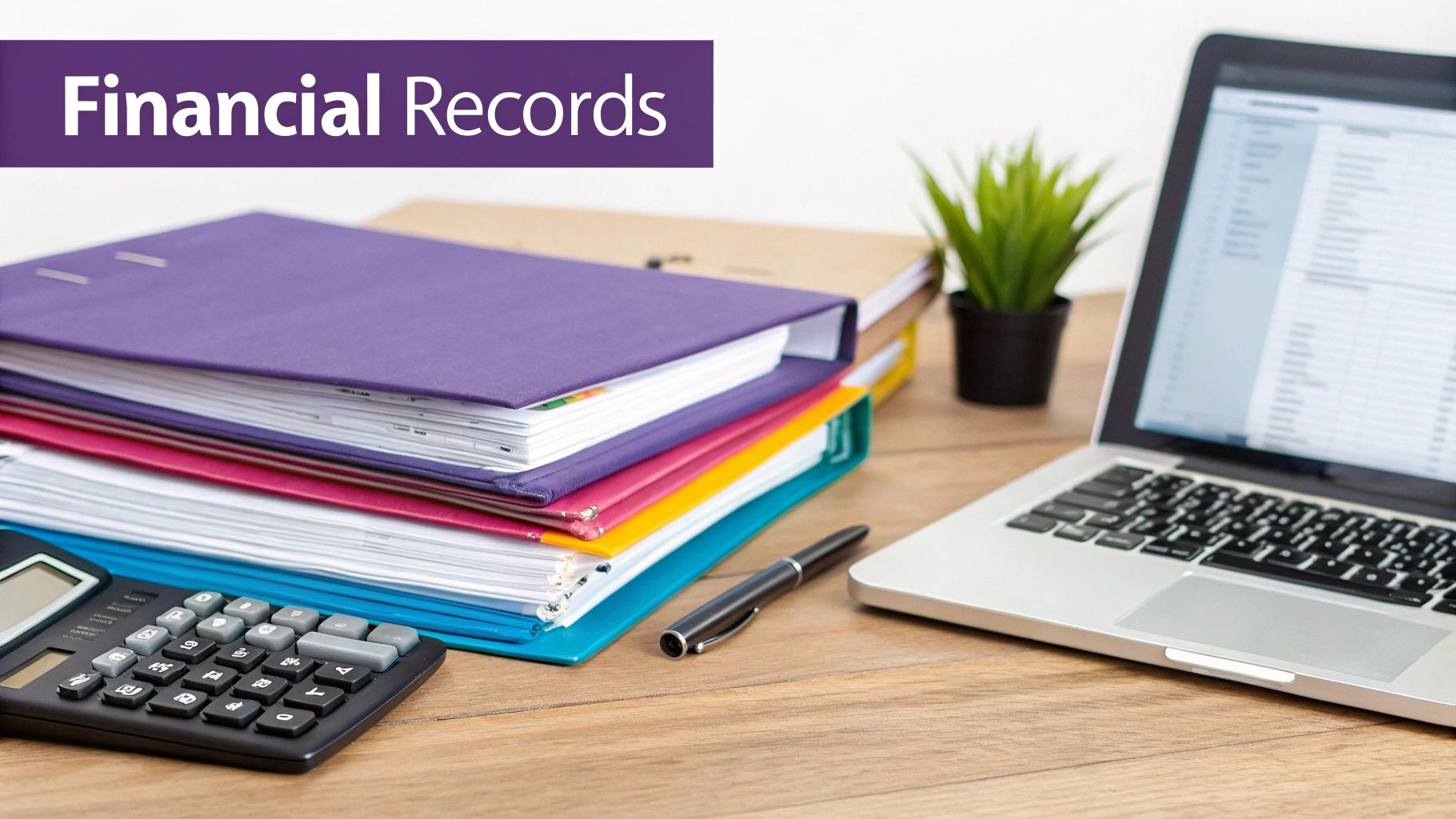 Stack of colorful financial records binders, calculator, pen, and laptop on a wooden desk.
