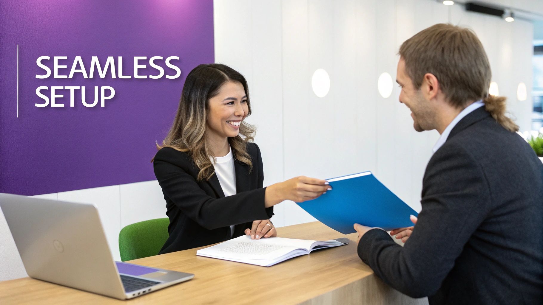 A smiling woman in a black blazer hands a blue folder to a man at a counter with a laptop, signifying a seamless setup.