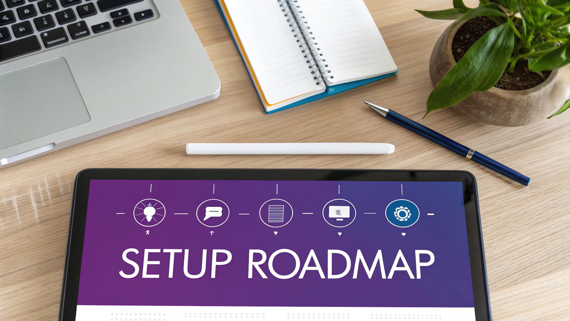 Overhead view of a workspace with a laptop, notebook, plant, pen, and tablet showing 'SETUP ROADMAP'.