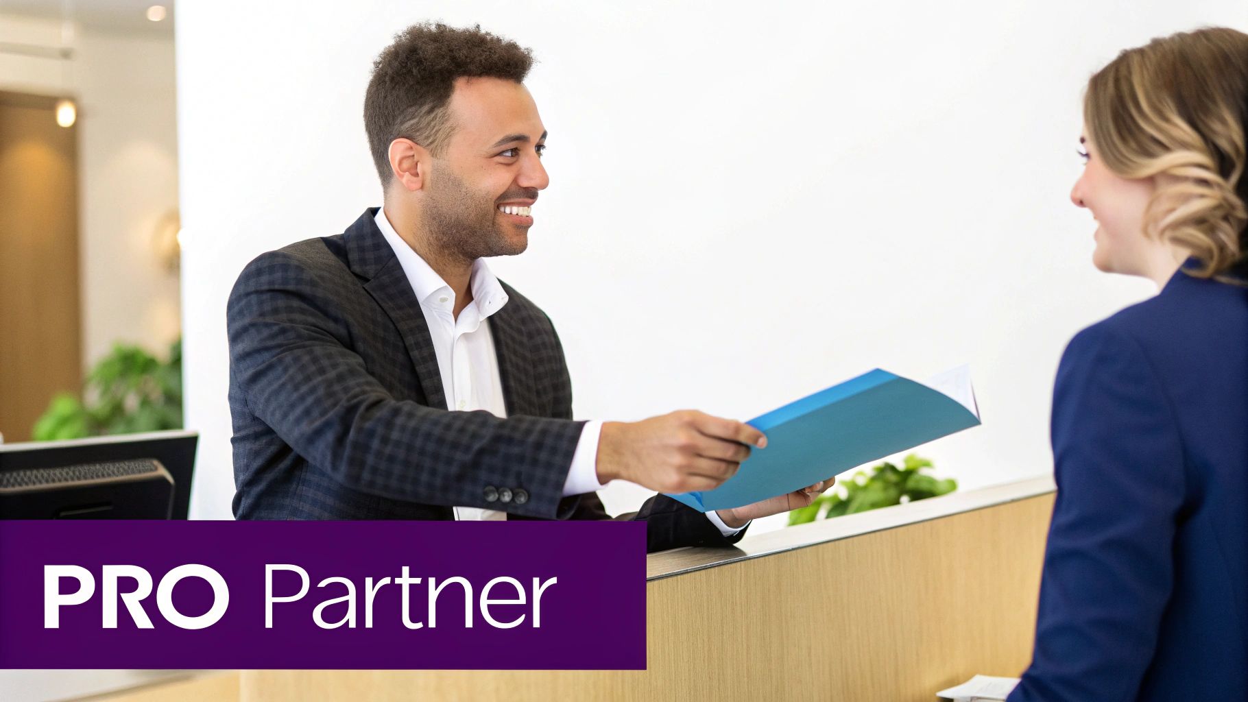 A smiling man in a suit hands a blue folder to a woman in a professional office setting.