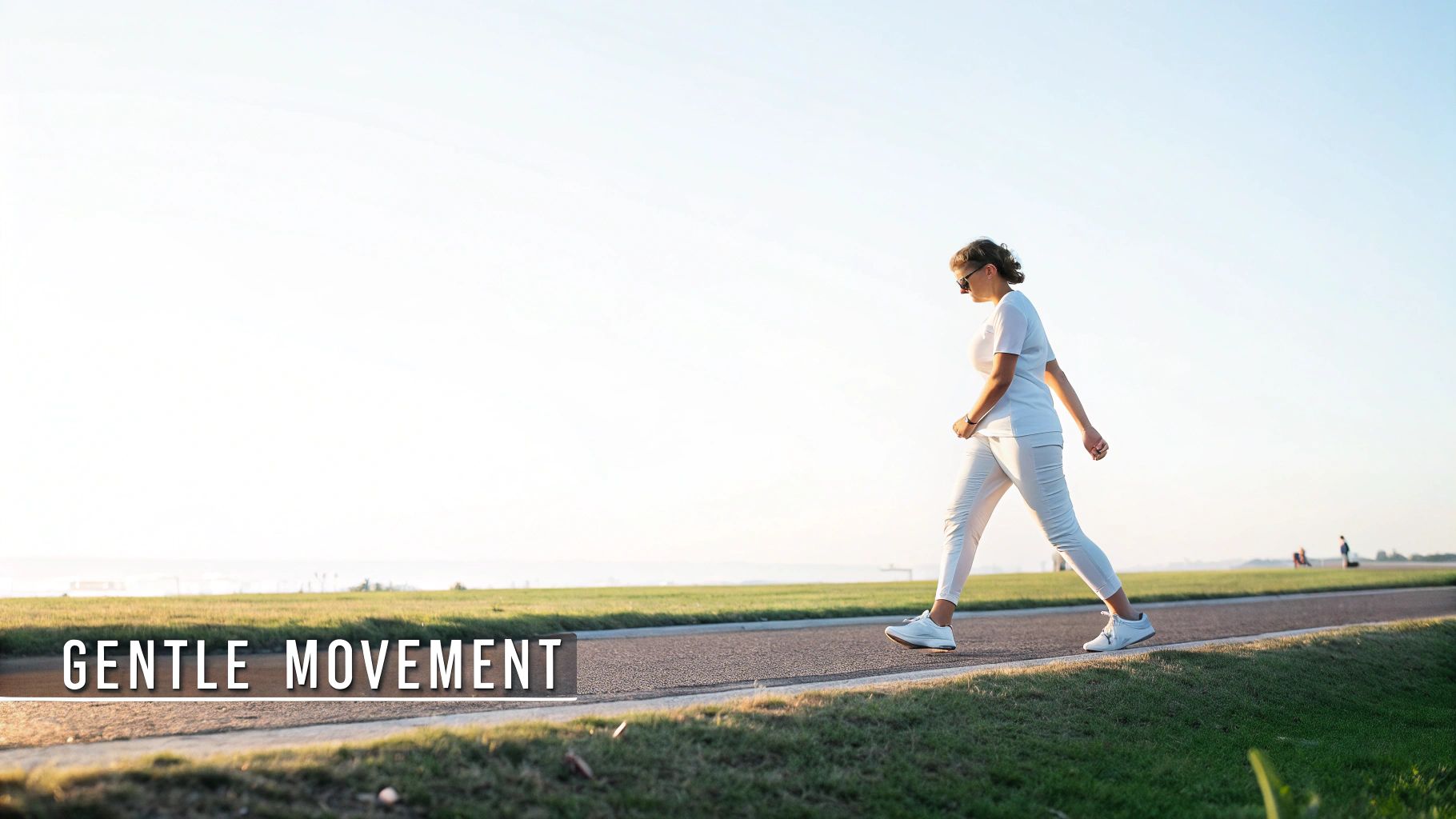 A woman in white clothing walking along a path next to green grass under a clear sky.