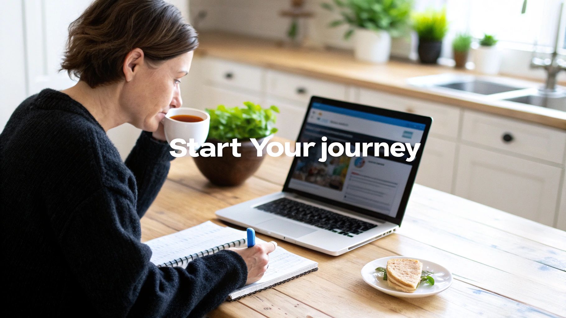 A woman sips coffee while writing in a notebook, with a laptop and sandwich on a wooden table.