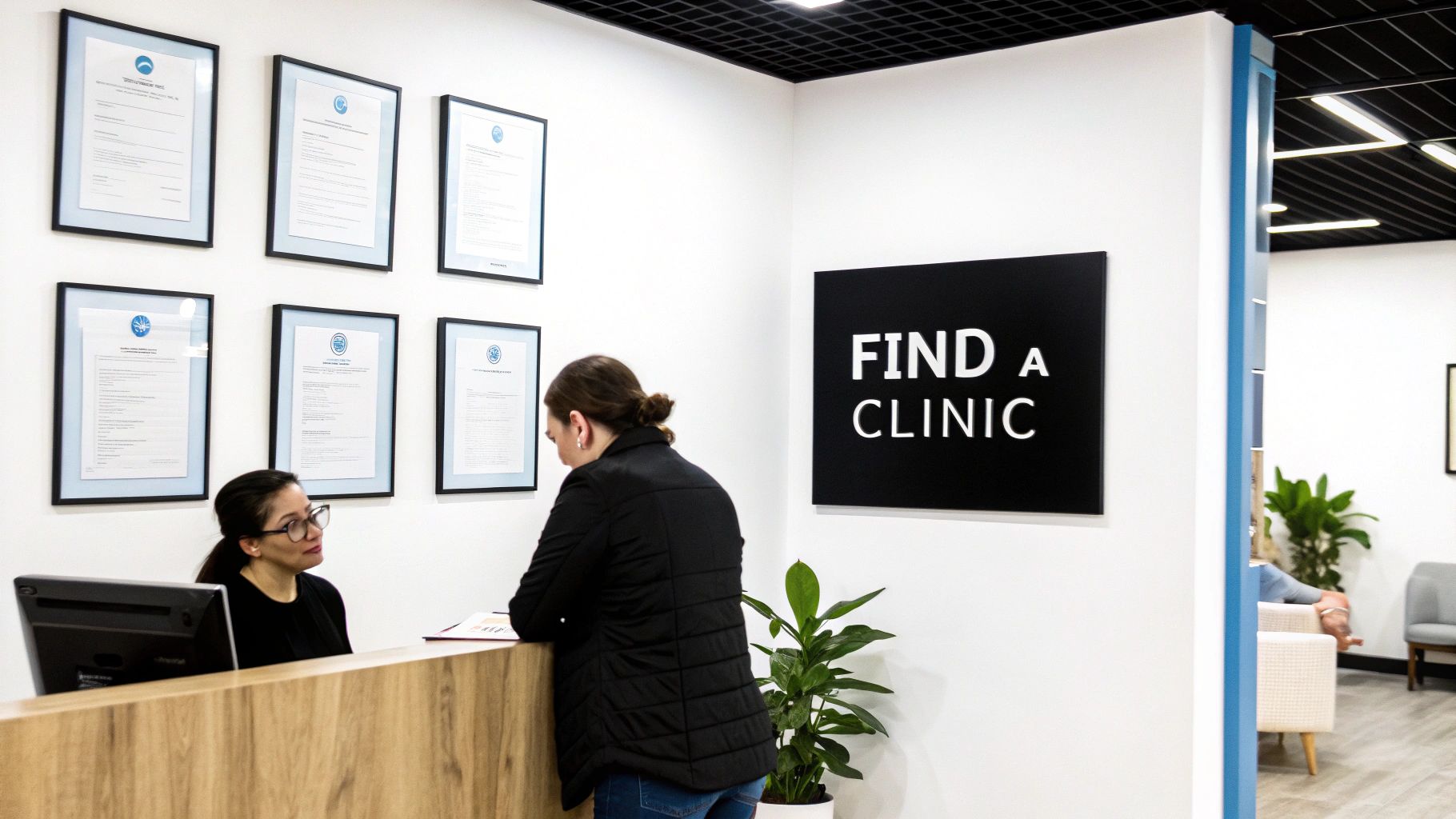 Two women at a modern clinic reception desk with framed certificates and a 'FIND A CLINIC' sign.