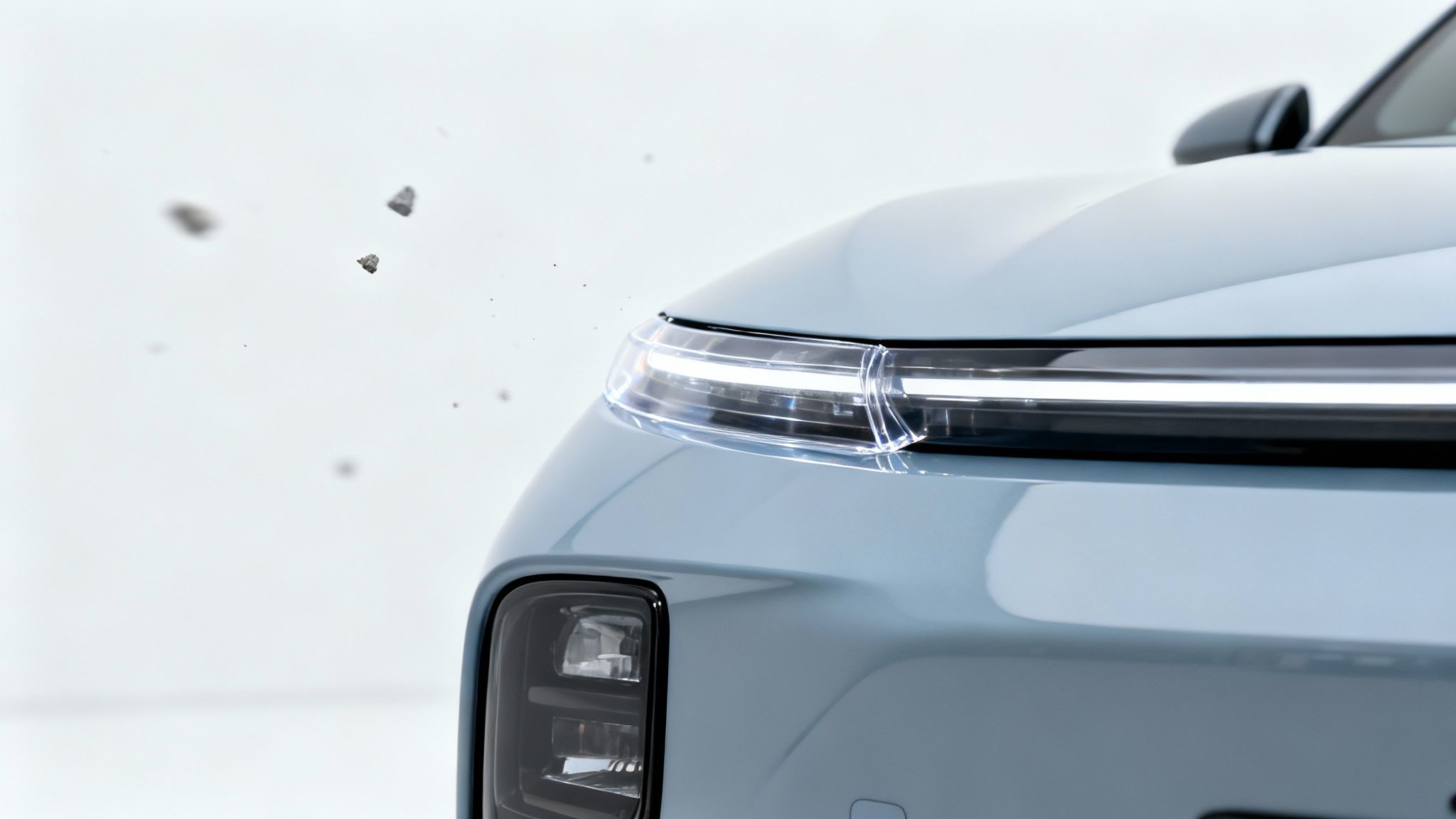 Close-up of a light blue car's front with illuminated LED lights and small debris in motion.