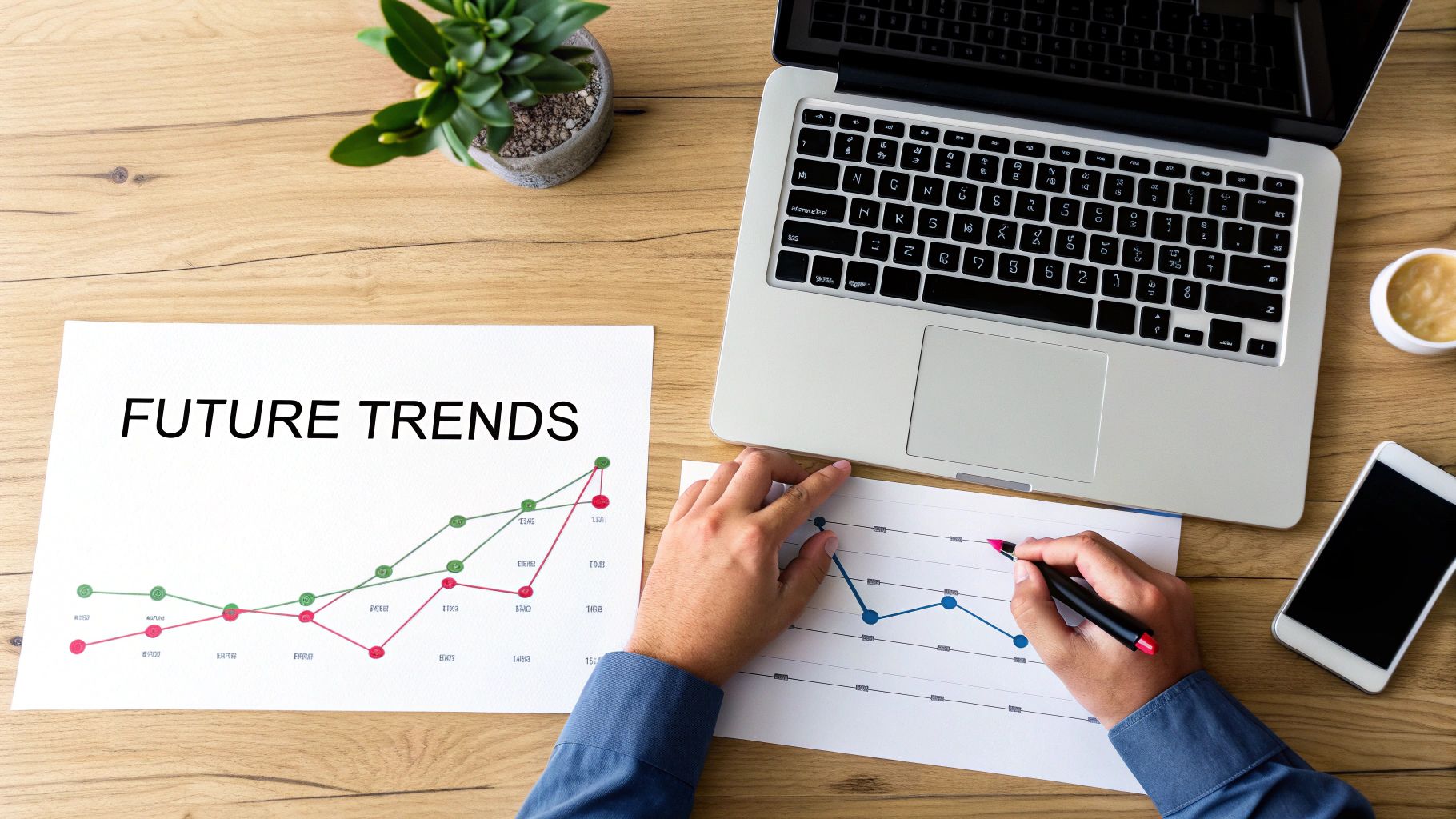 Overhead shot of a person analyzing future trends on graphs with a laptop and smartphone on a wooden desk.