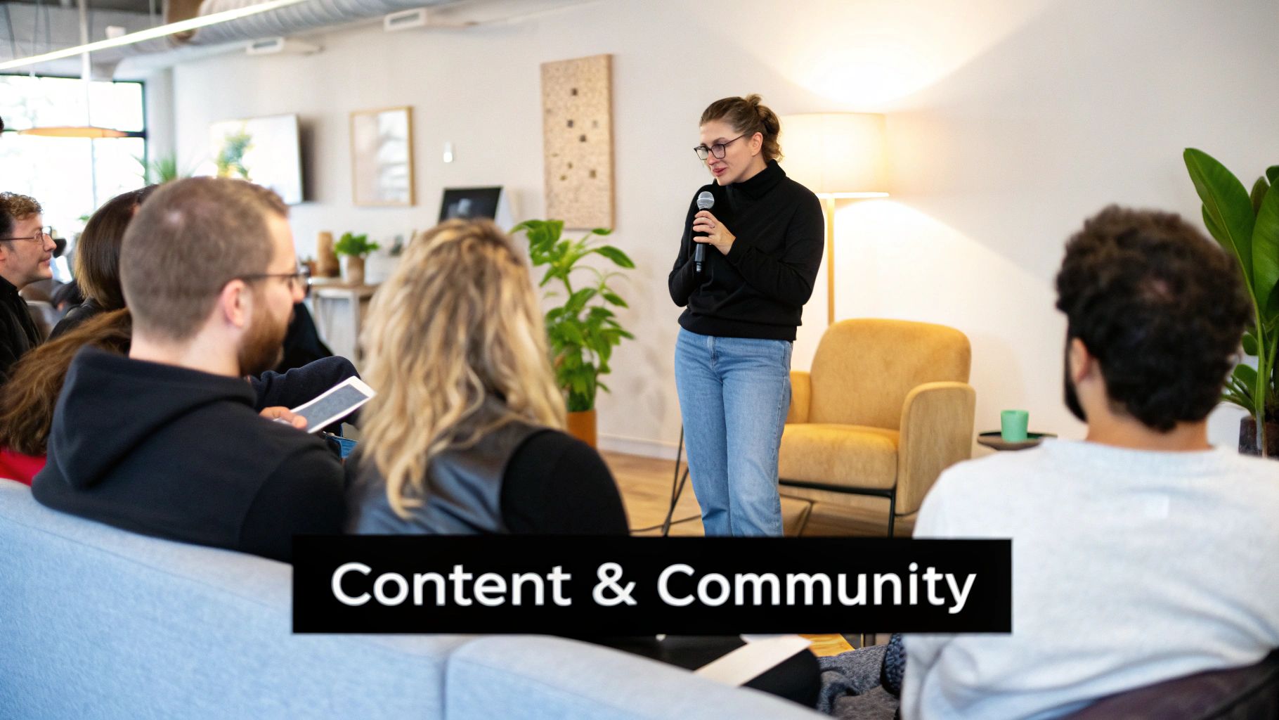 A woman speaks into a microphone to an audience seated on couches at a Content & Community event.