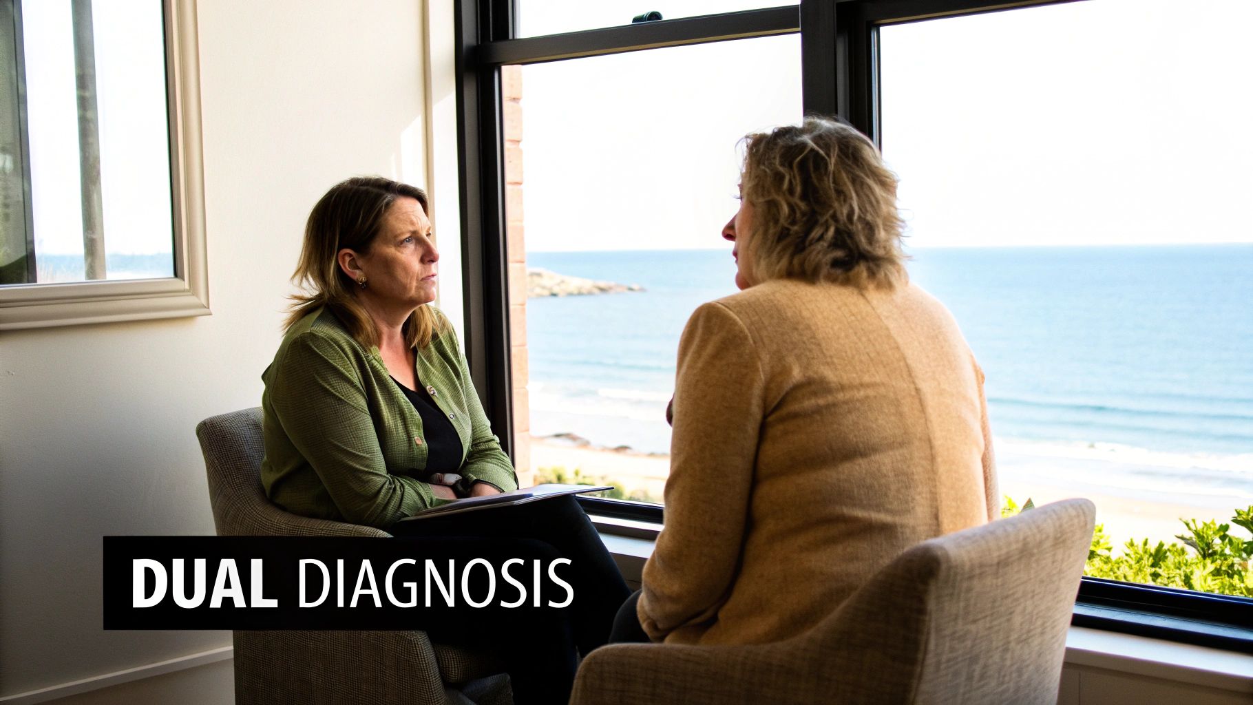 Two women discuss dual diagnosis treatment in a room with an ocean view.