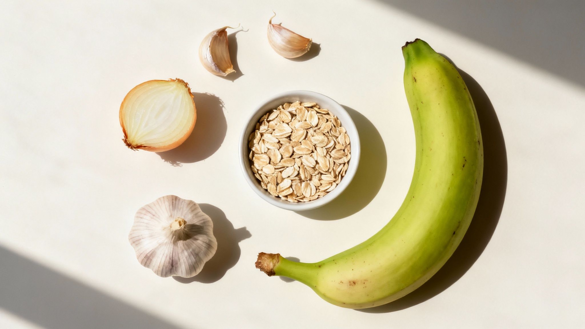 A variety of prebiotic foods like garlic, onions, bananas, and oats arranged neatly on a wooden surface.