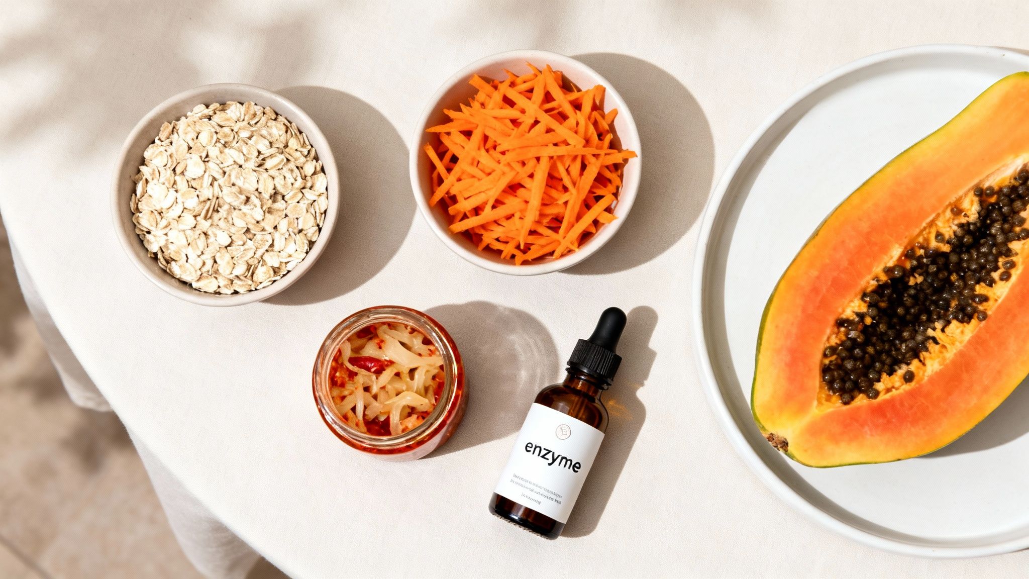 Overhead shot of oats, shredded carrots, pickled vegetables, papaya, and an enzyme supplement bottle.