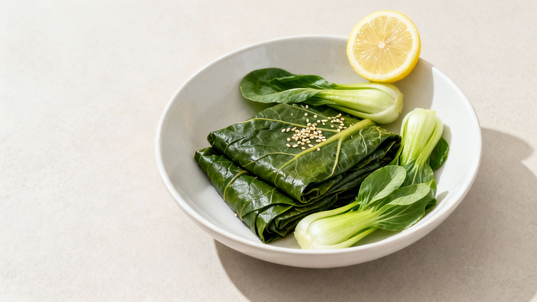 A bowl of healthy green collard greens wraps with sesame seeds, bok choy, and a lemon half.