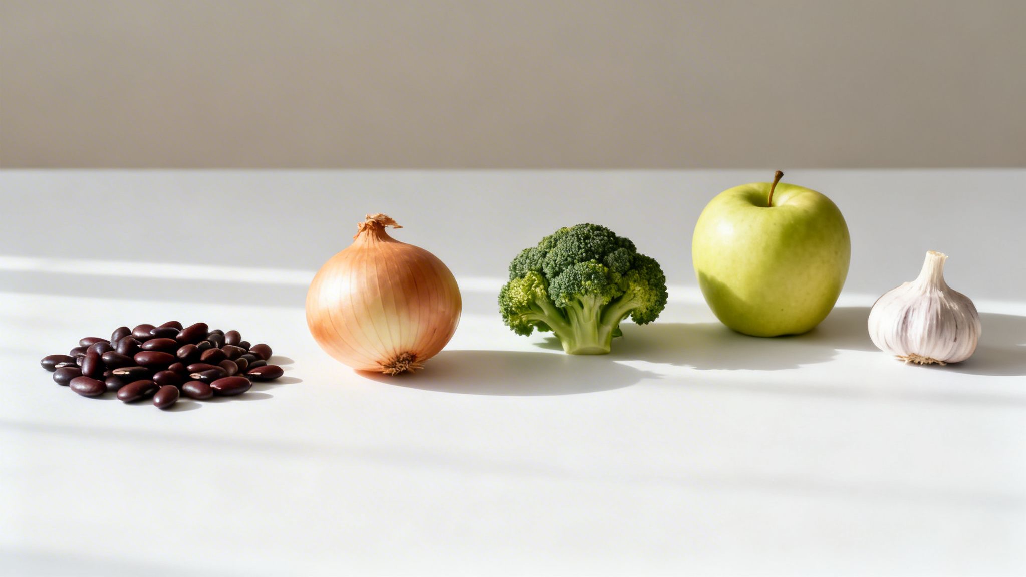 A line of healthy ingredients: beans, onion, broccoli, green apple, and garlic on white.