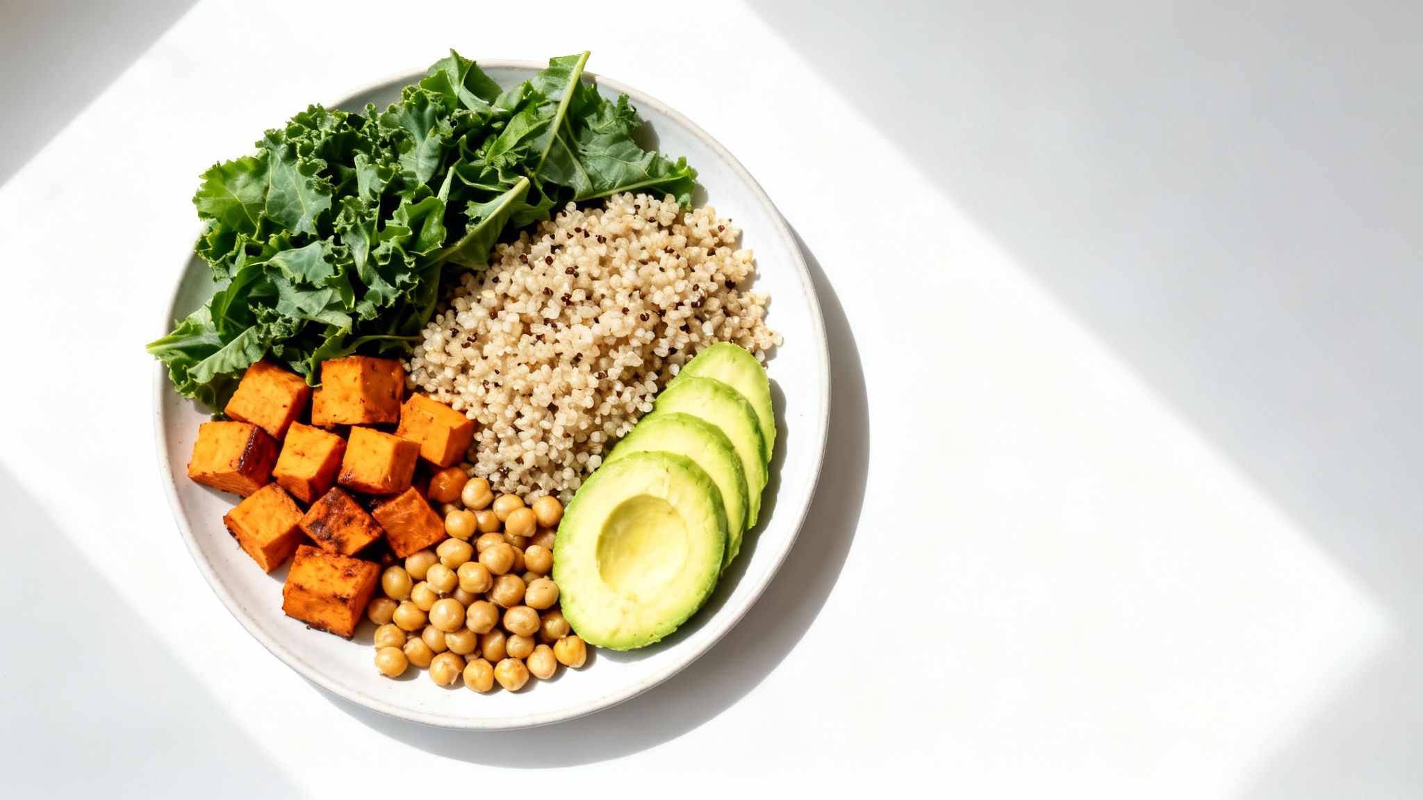 A vibrant plant-based Buddha bowl featuring kale, quinoa, sweet potatoes, chickpeas, and avocado slices.