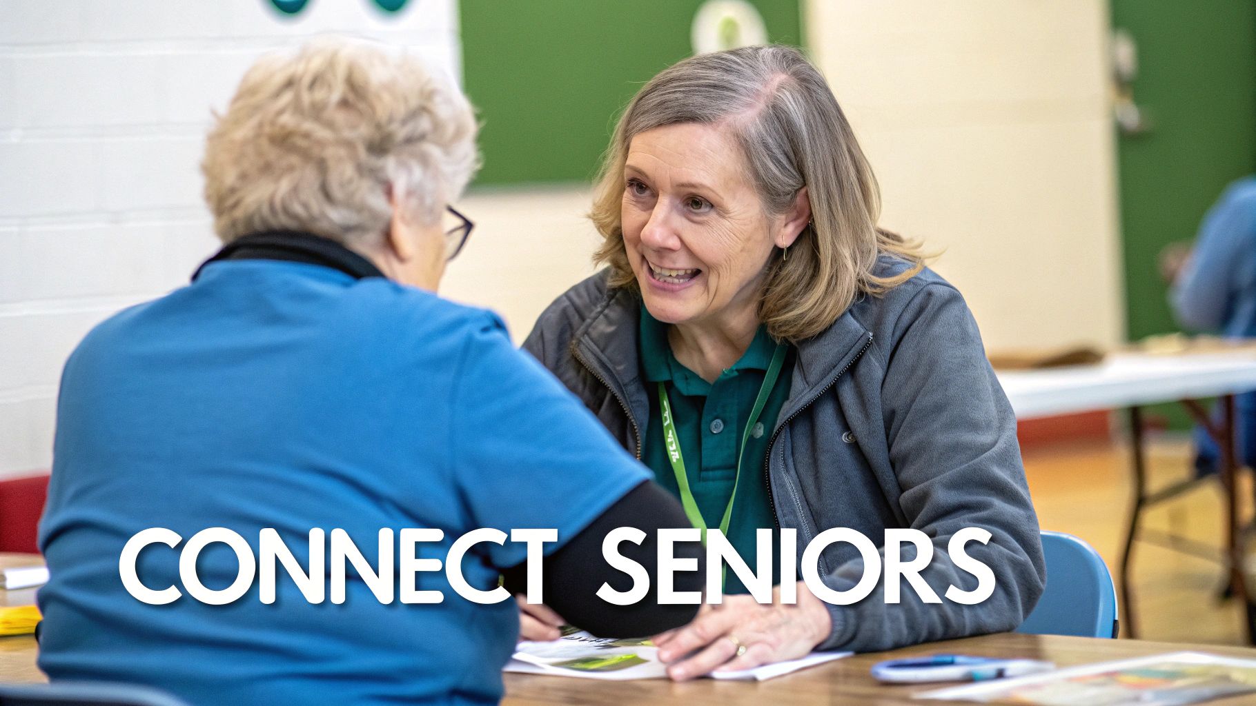 An older woman in a grey jacket and green shirt smiles while talking to another senior.