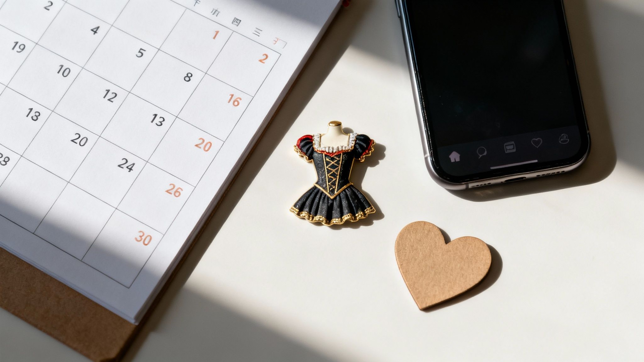 Calendar and smartphone on desk with decorative dress pin and heart symbolizing webcam modeling schedule