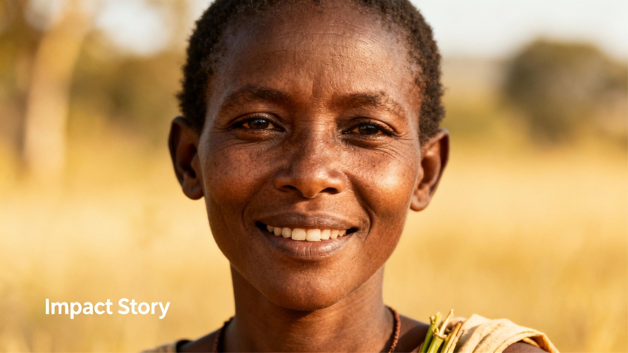 A joyful African woman with a bright smile looks directly at the camera in a sunny outdoor setting.