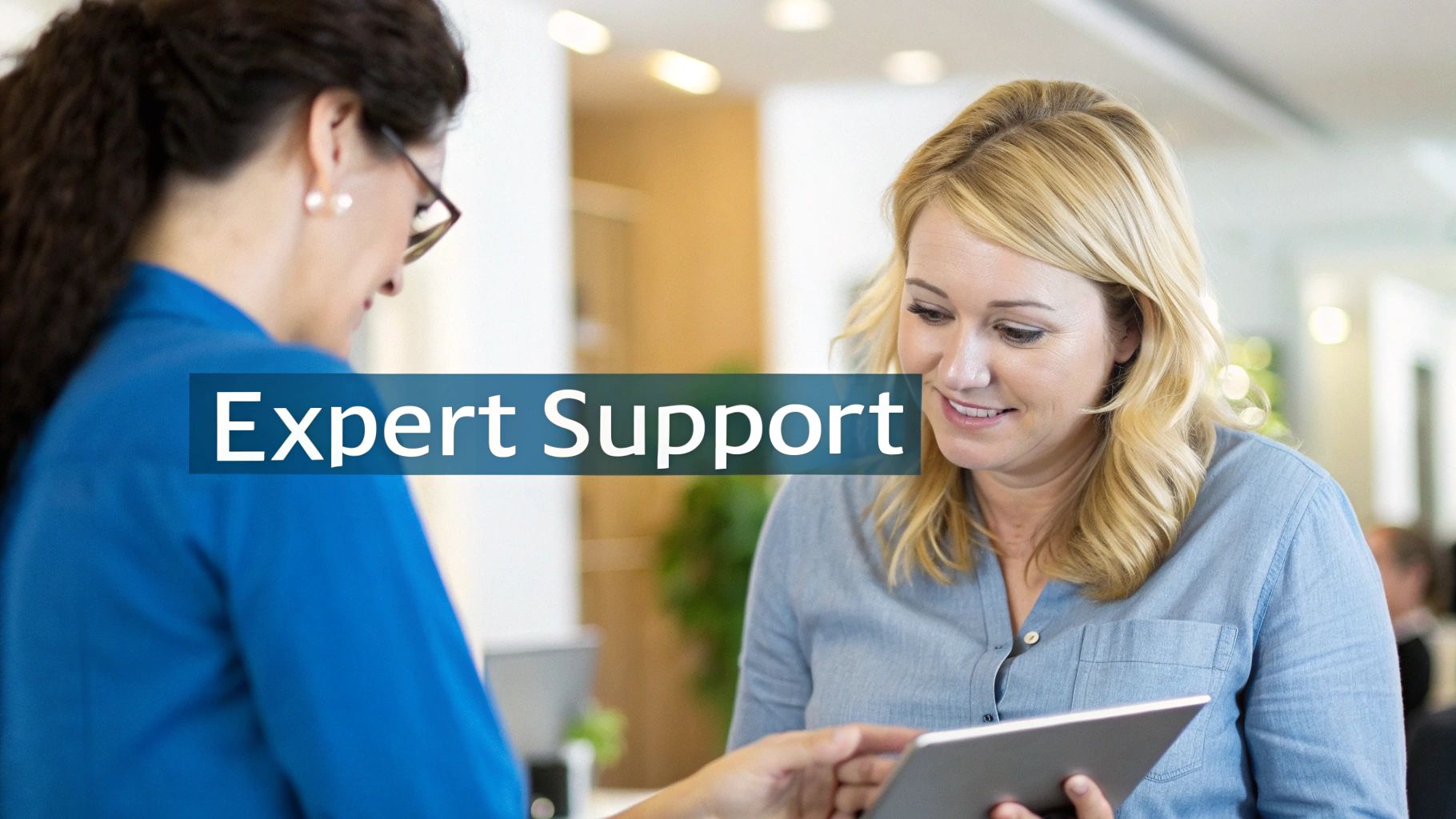 Two professional women collaborating and discussing content on a digital tablet, representing expert support.