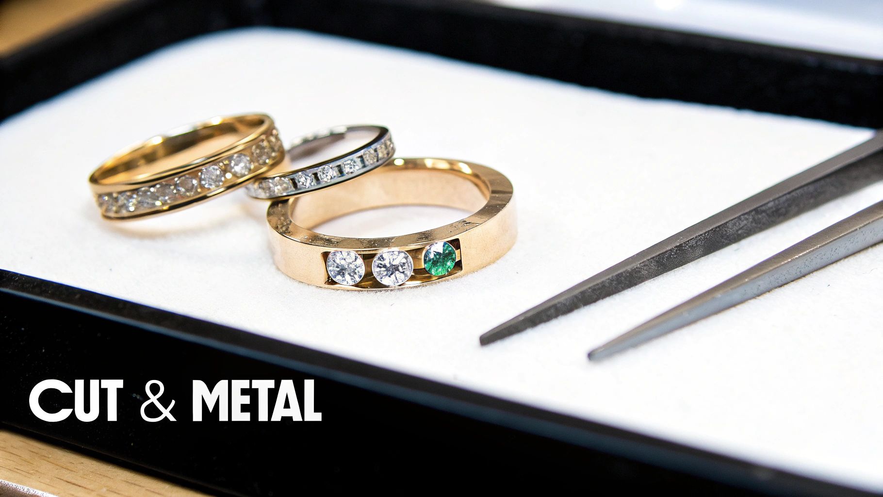 Three gold and diamond rings, one with an emerald, displayed in a black jewelry tray with jeweler's tools.