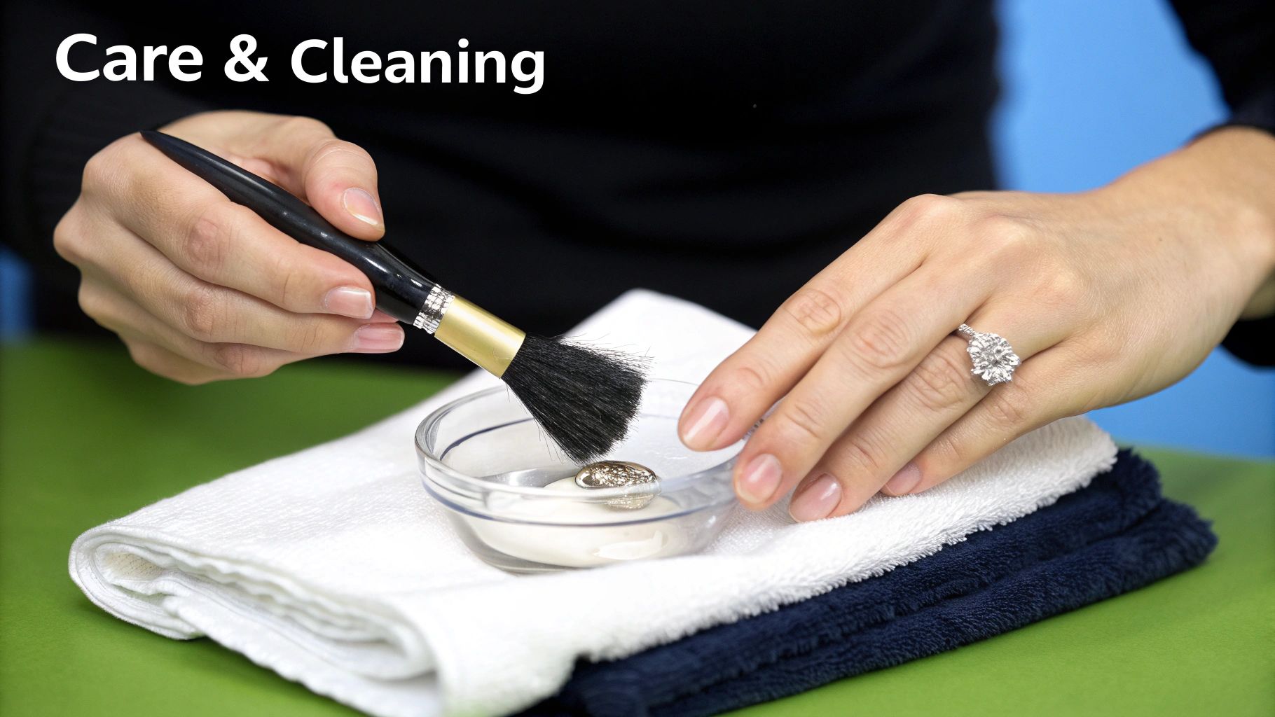 A person uses a brush to clean a sparkling piece of jewelry in a small dish, with towels nearby.