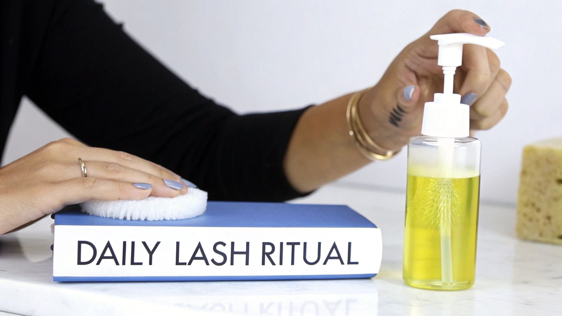 A person's hands performing a daily lash ritual, pumping cleanser onto a soft pad.