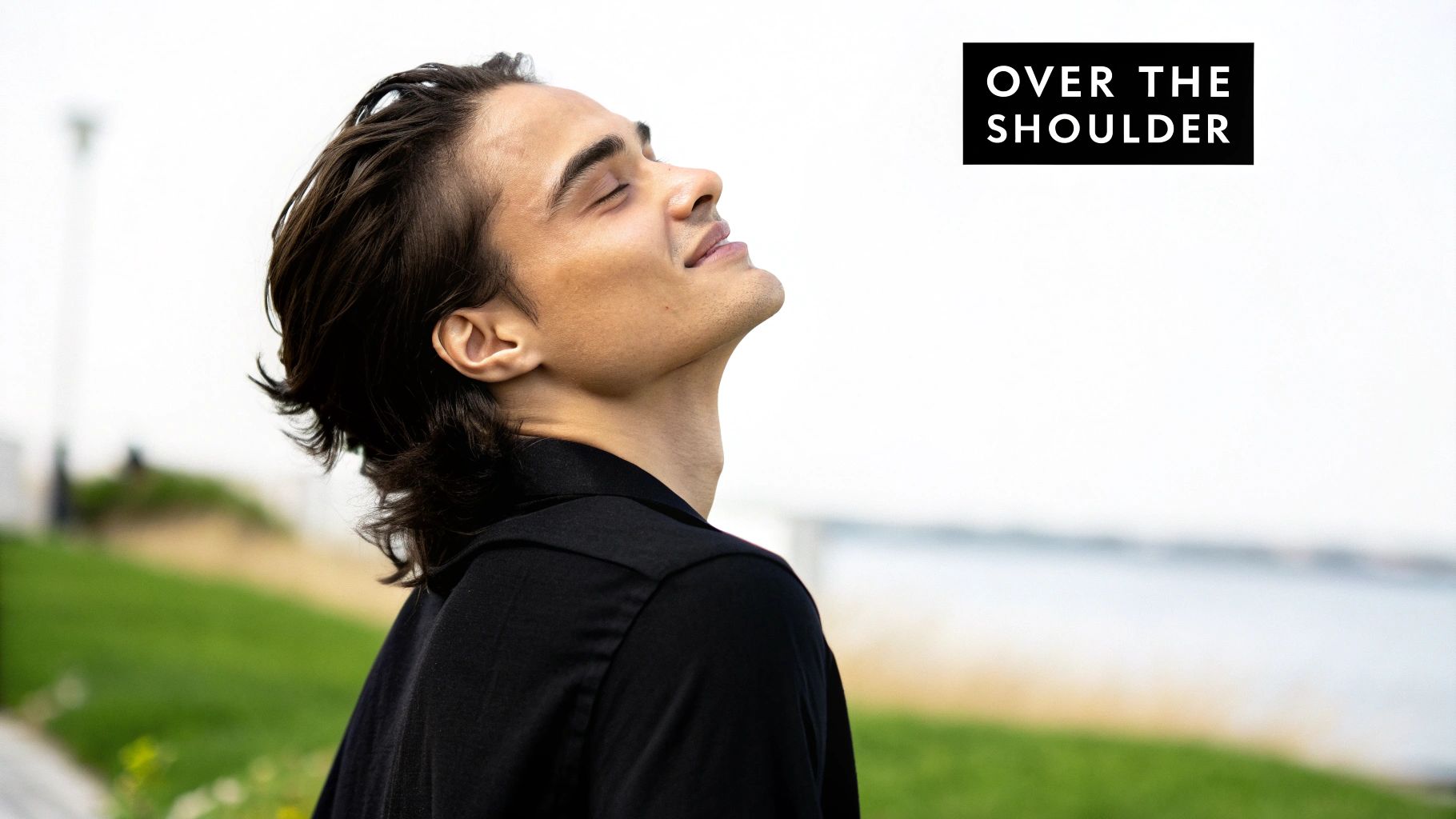 A young man with dark hair in a black shirt looks up with closed eyes enjoying the outdoors.