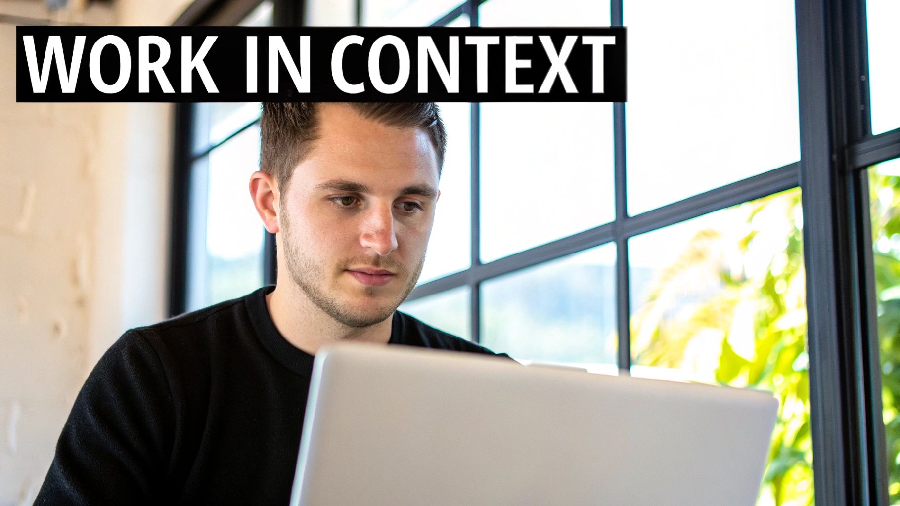 Young man working intently on a silver laptop in a bright office setting.