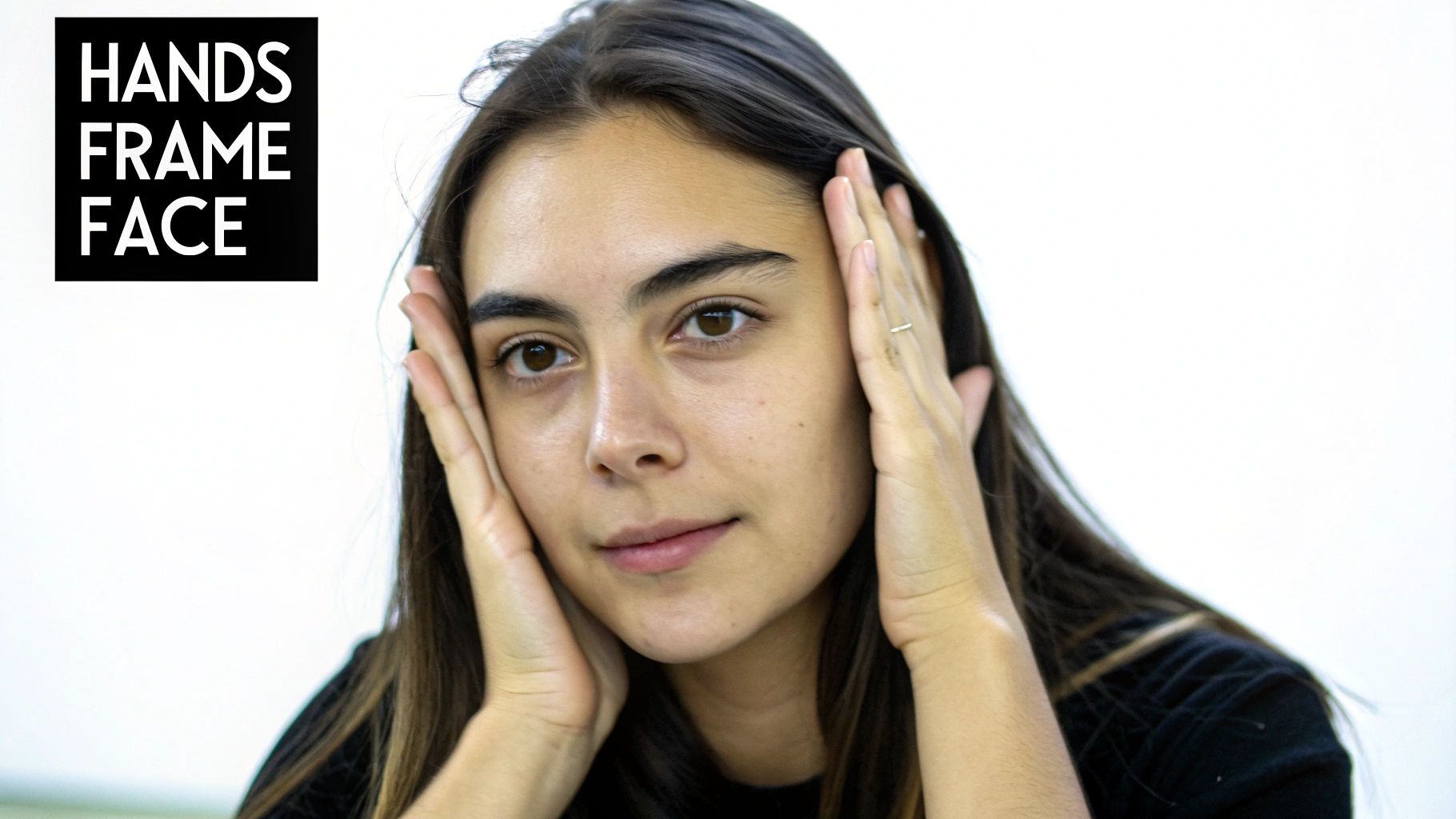 Close-up of a young woman with dark hair framing her face with both hands.