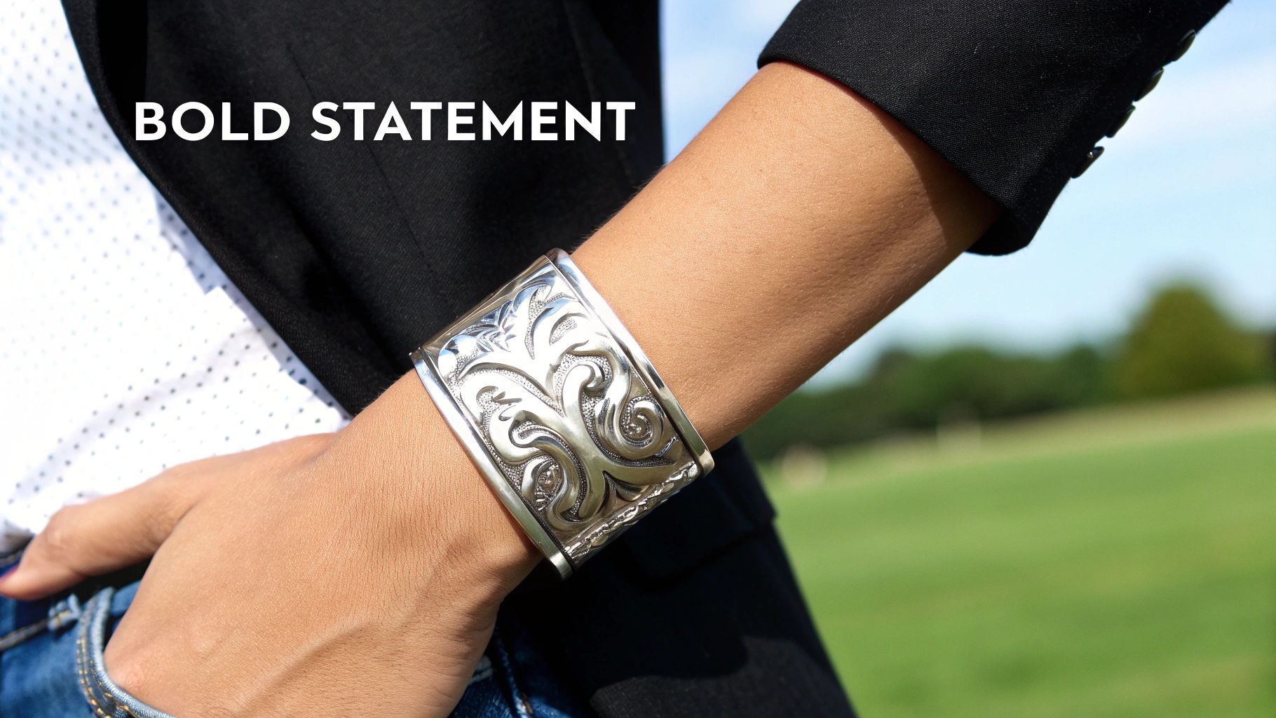 A person wears a large, ornate silver cuff bracelet with a black blazer, white shirt, and blue jeans.
