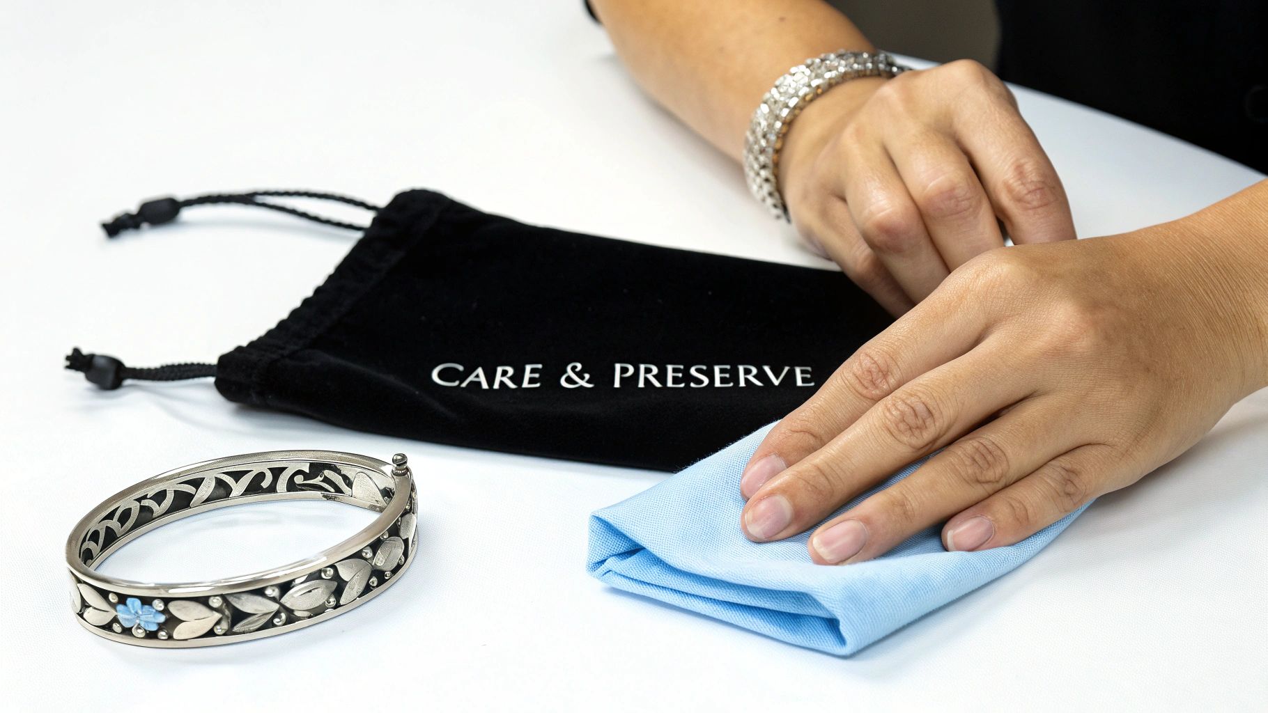 Hands cleaning an ornate silver bangle bracelet with a blue cloth and a 'Care & Preserve' pouch.