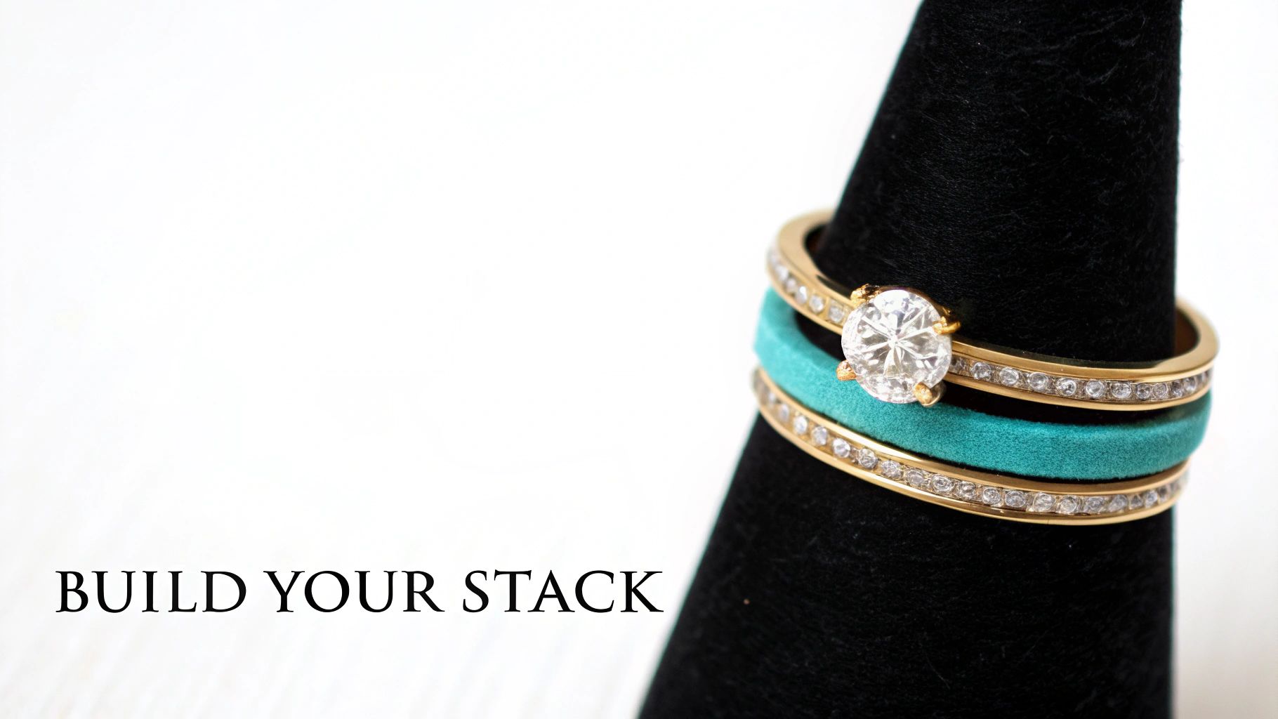 A dazzling stack of gold and diamond rings, including a solitaire and eternity bands, with a teal accent band on a black display.