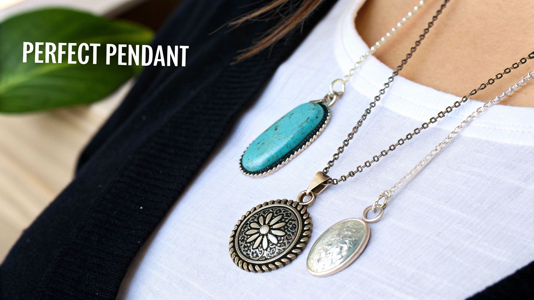 A person wears three layered necklaces with diverse pendants: turquoise, floral, and an oval design.